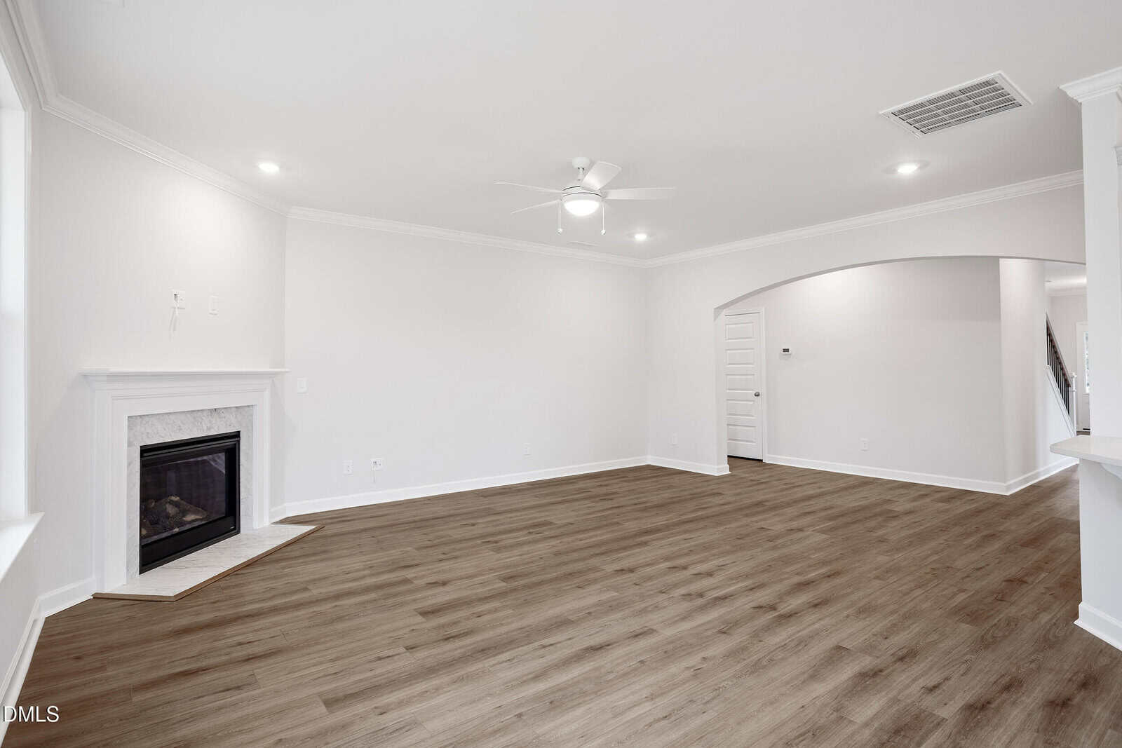 Spacious living room with light walls, wood-look flooring, a white ceiling fan, recessed lighting, and a fireplace in the corner. An arched doorway leads to another room. The space is empty and unfurnished.