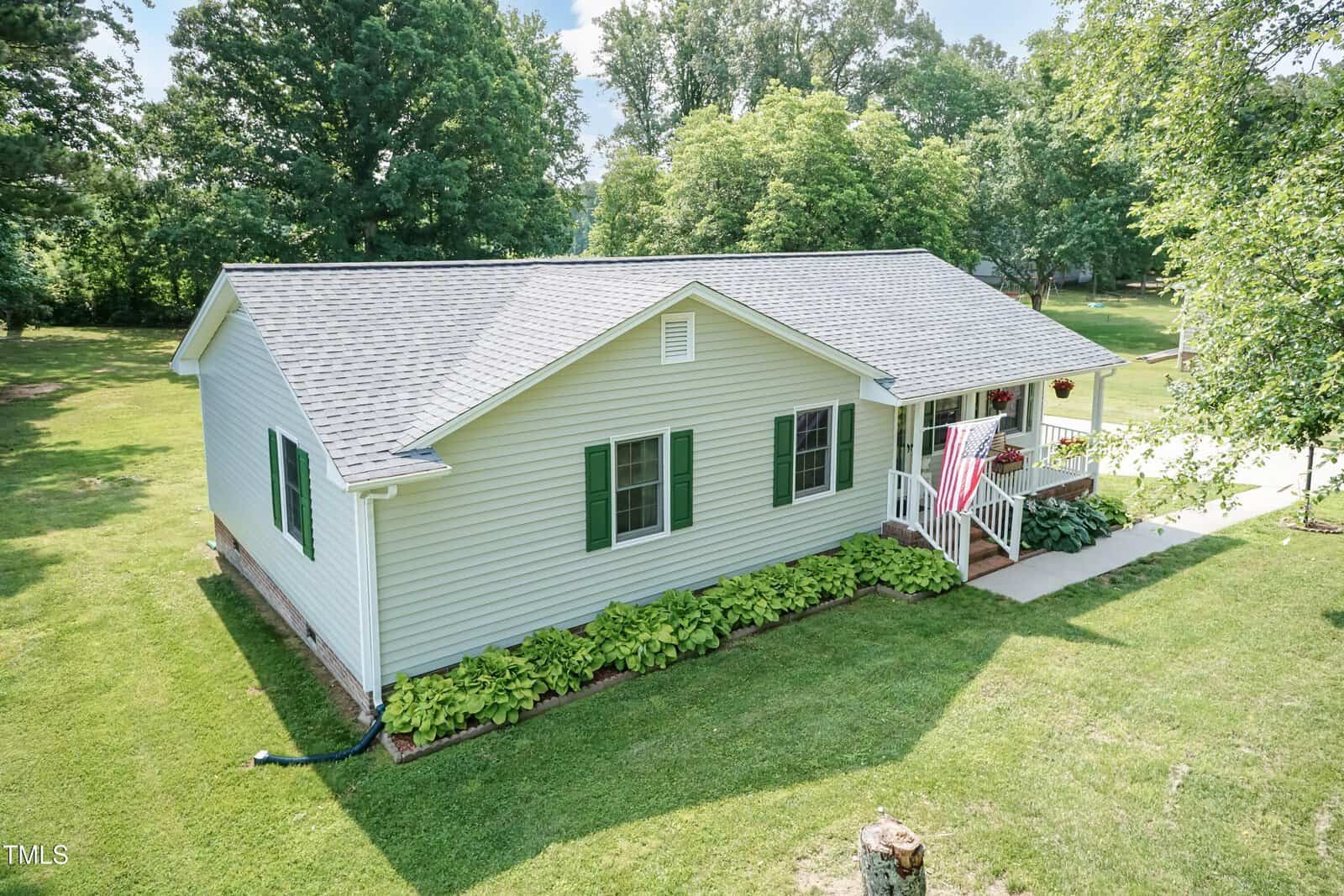A single-story house at 523 Edwards Road in Henderson features light-colored siding, green shutters, and a small front porch with an American flag. The home sits among mature trees and a grassy lawn under a partly cloudy sky.