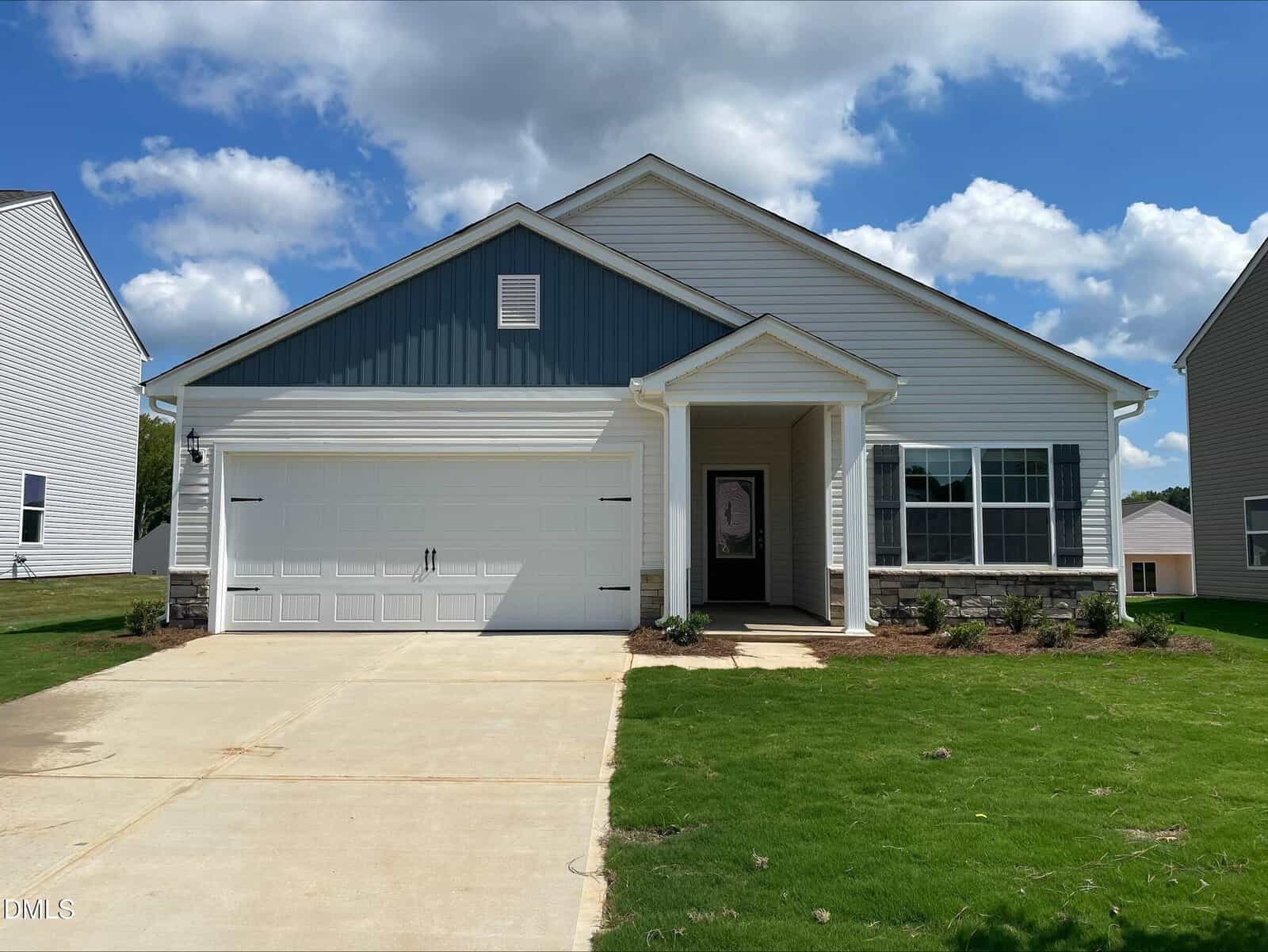 Single-story house with white and blue siding at 104 Old Arcadia Lane, featuring a double garage door, a small covered entryway, front lawn, and concrete driveway under a partly cloudy sky. Neighboring houses in Youngsville are visible on both sides.