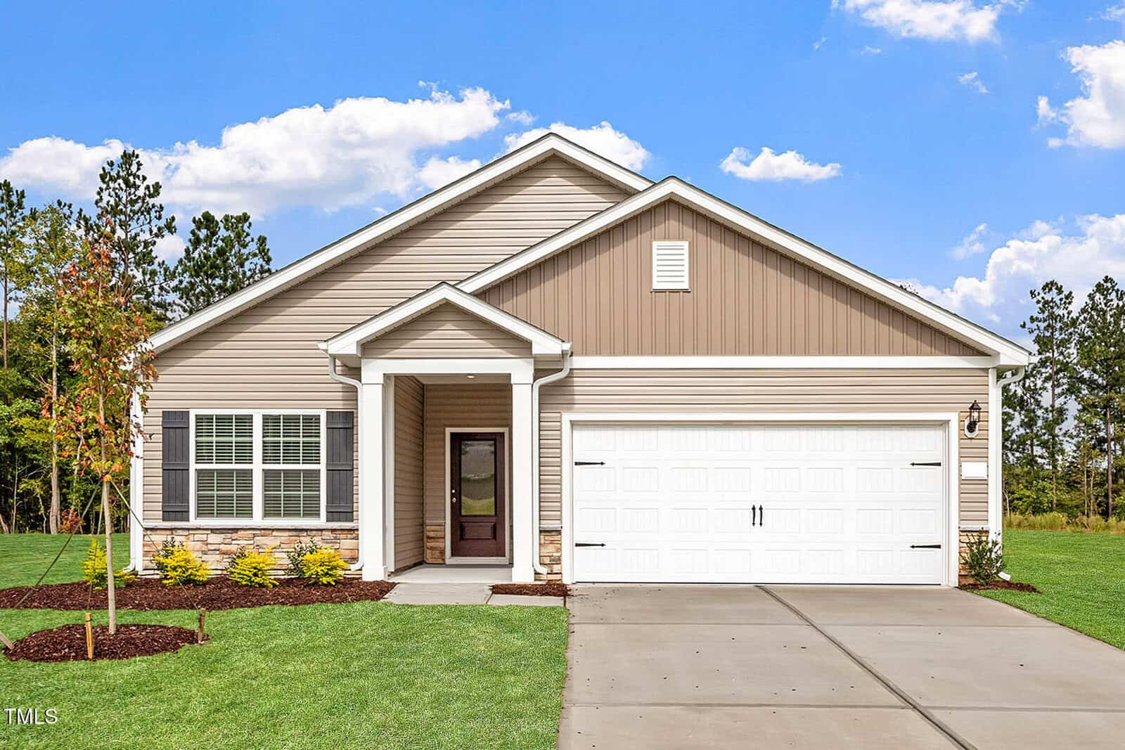 A single-story house at 405 Benton Drive, Oxford, features tan siding, white trim, a two-car garage, stone accents, a covered entryway, and a concrete driveway. The front yard offers green grass, new landscaping, and a young tree.