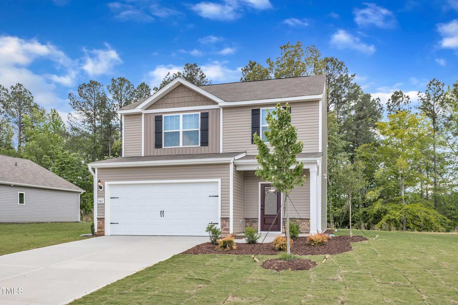 Located at 106 Flue Court in Oxford, this two-story beige house with white trim features a double garage, a concrete driveway, and a lush lawn with young trees and shrubs set against tall trees under a clear blue sky.