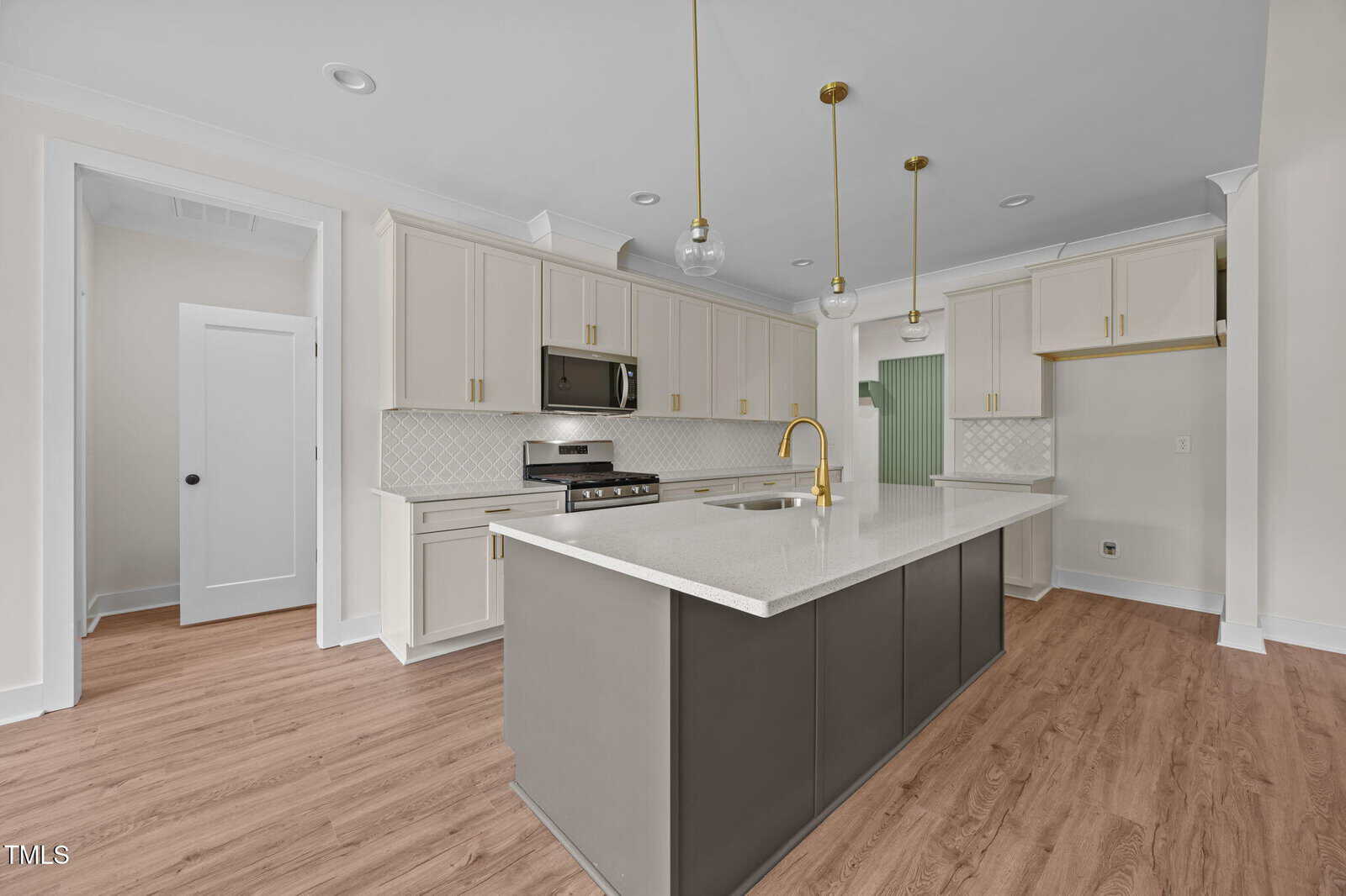 Modern kitchen with white cabinets, a large gray island with a white countertop, gold fixtures, pendant lights, stainless steel appliances, and light wood flooring.