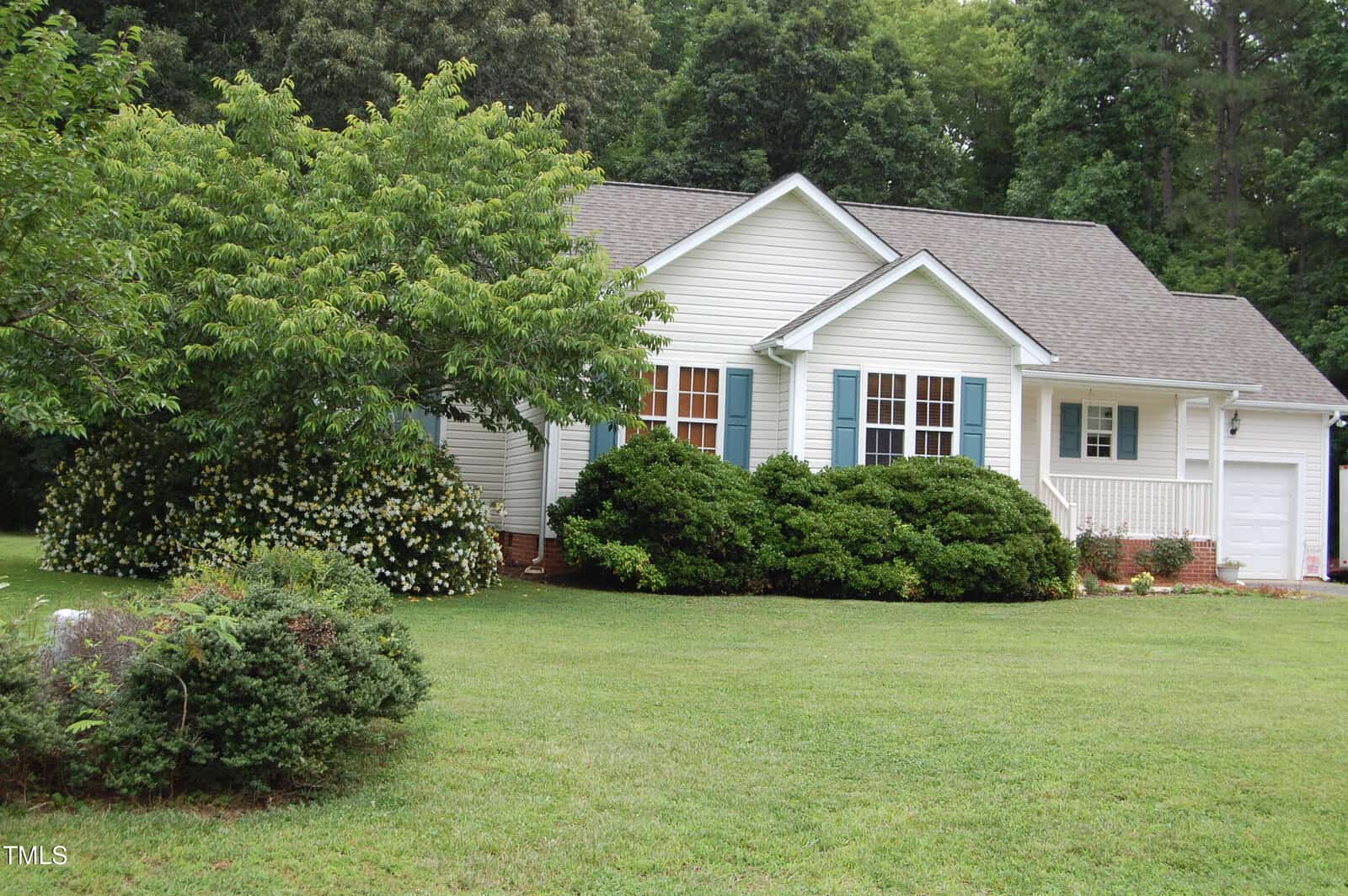 A single-story white house with blue shutters at 3145 Pier Pointe Drive, Creedmoor, is surrounded by green bushes and trees, sitting on a well-maintained lawn with a driveway and attached garage on the right.