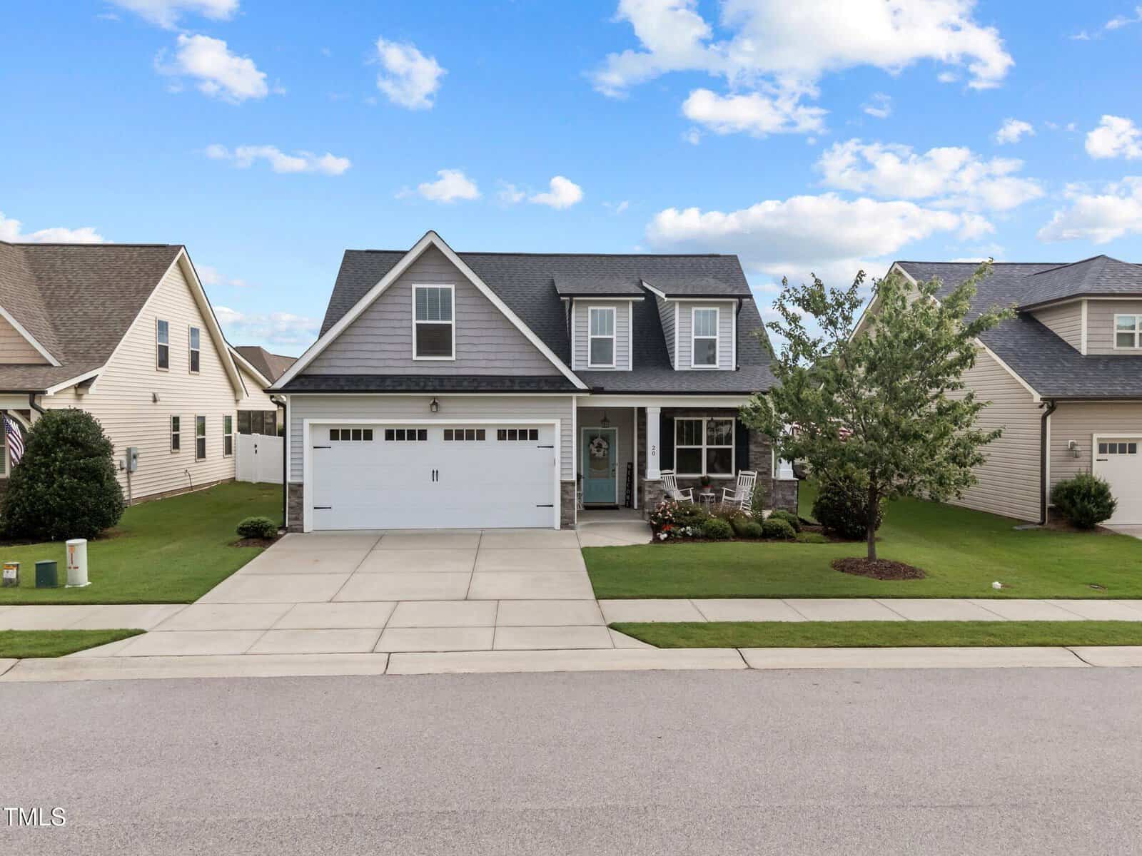 A modern two-story gray house with a white garage, front porch, and well-kept lawn, set in a suburban neighborhood under a blue sky with scattered clouds.