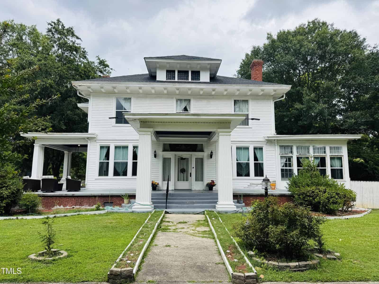 A large two-story white house with tall columns stands at 275 Gholson Avenue, Henderson. It features a covered front porch, black roof, multiple windows, well-kept lawn with shrubs, a concrete path to the entrance, and trees in the background.