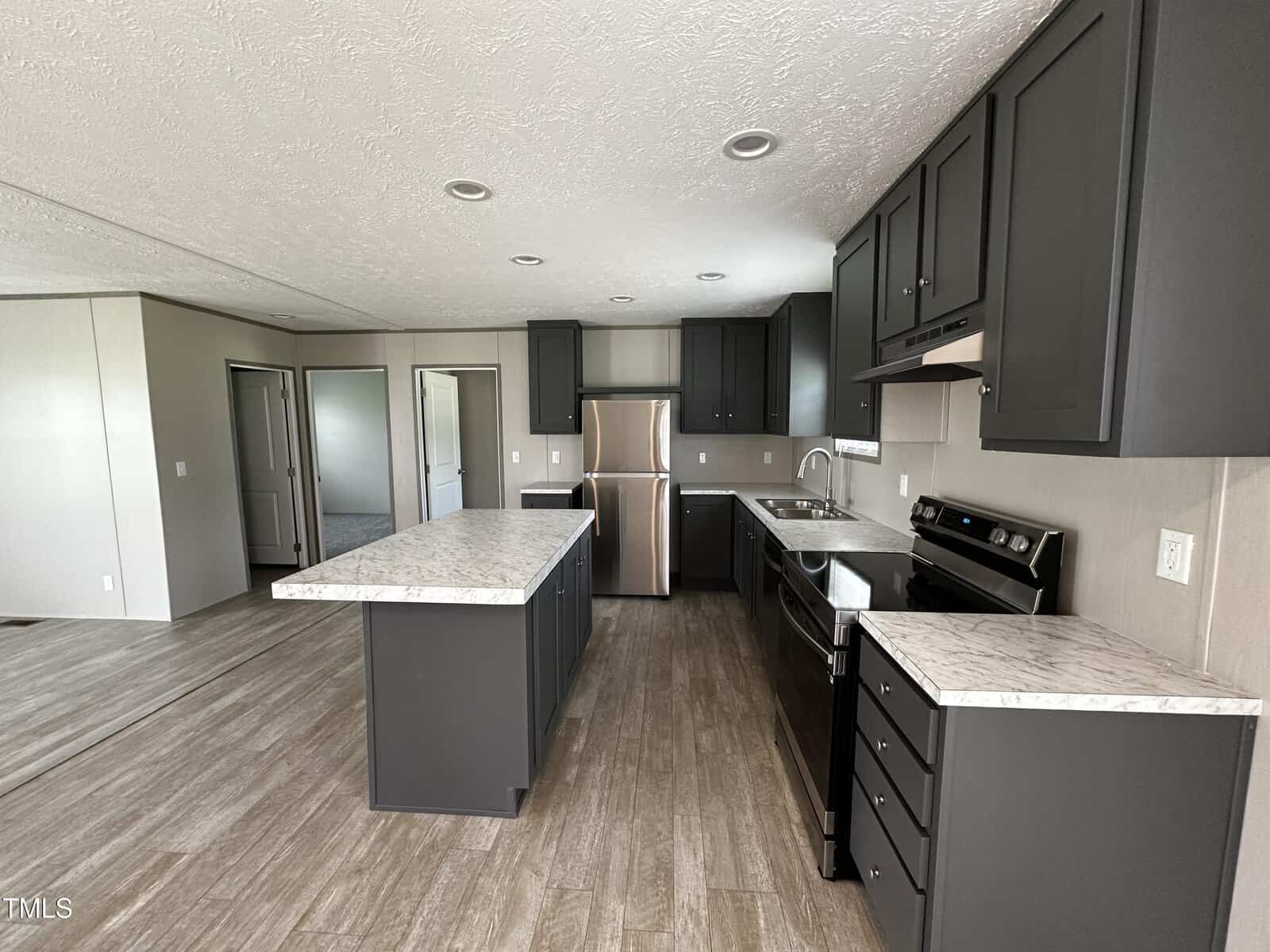 Modern kitchen with dark gray cabinets, stainless steel appliances, a central island, marble-look countertops, and wood-style flooring. Open layout connects to additional rooms visible in the background.