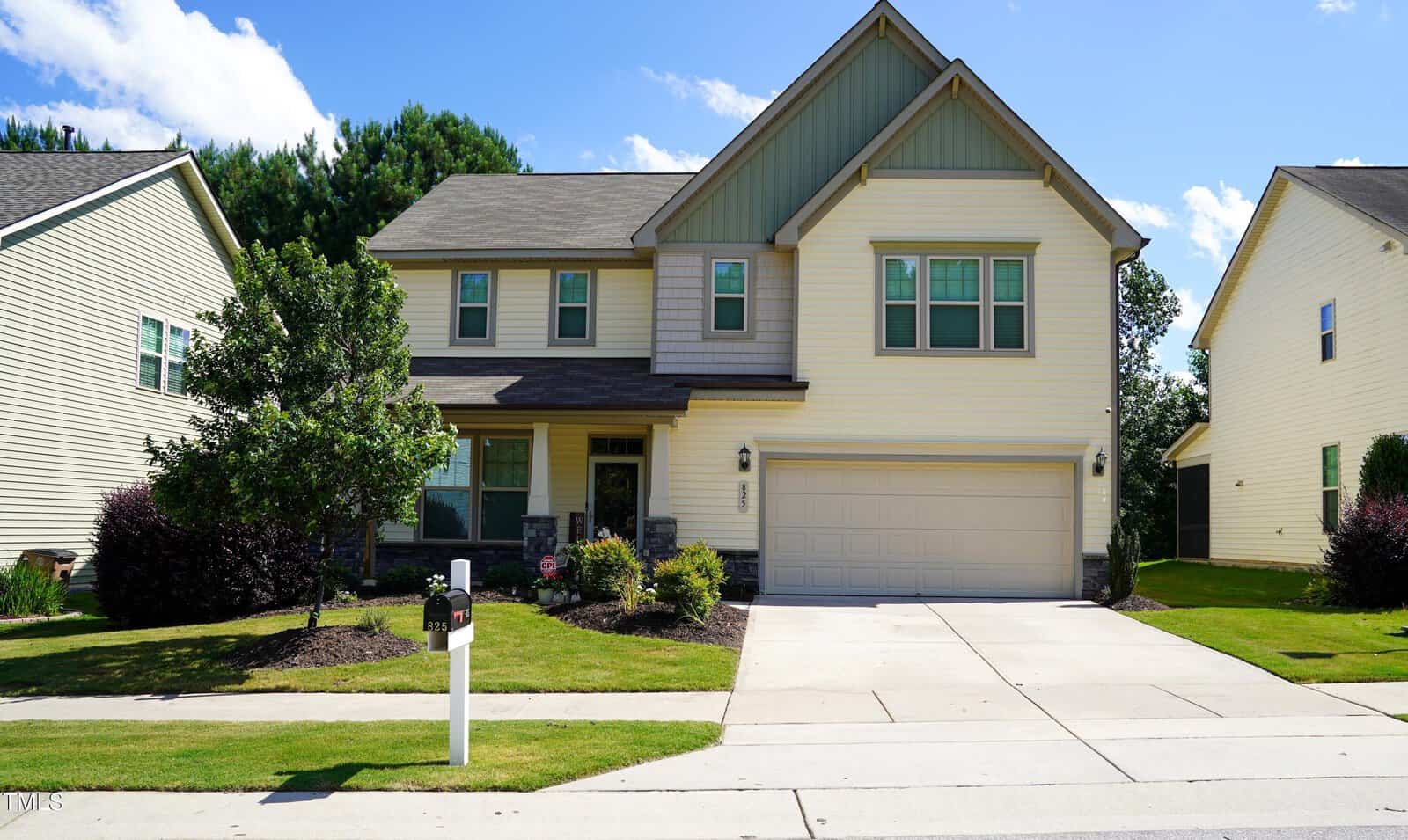 Two-story suburban house with beige siding, green accents, and a two-car garage located at 825 Fulworth Avenue in Wake Forest. The front yard has trimmed grass, shrubs, small trees, and a white mailbox near the driveway. Neighboring houses are visible on both sides.