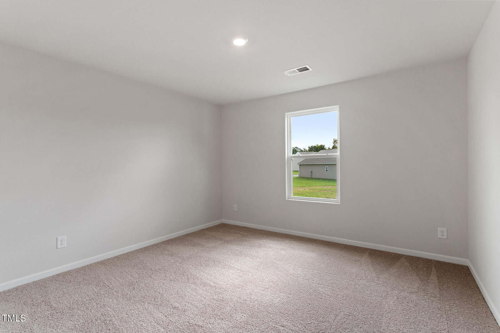 Empty, carpeted room with beige walls, a single window showing a grassy yard and neighboring building, and a ceiling light. The room appears clean, bright, and minimalistic.