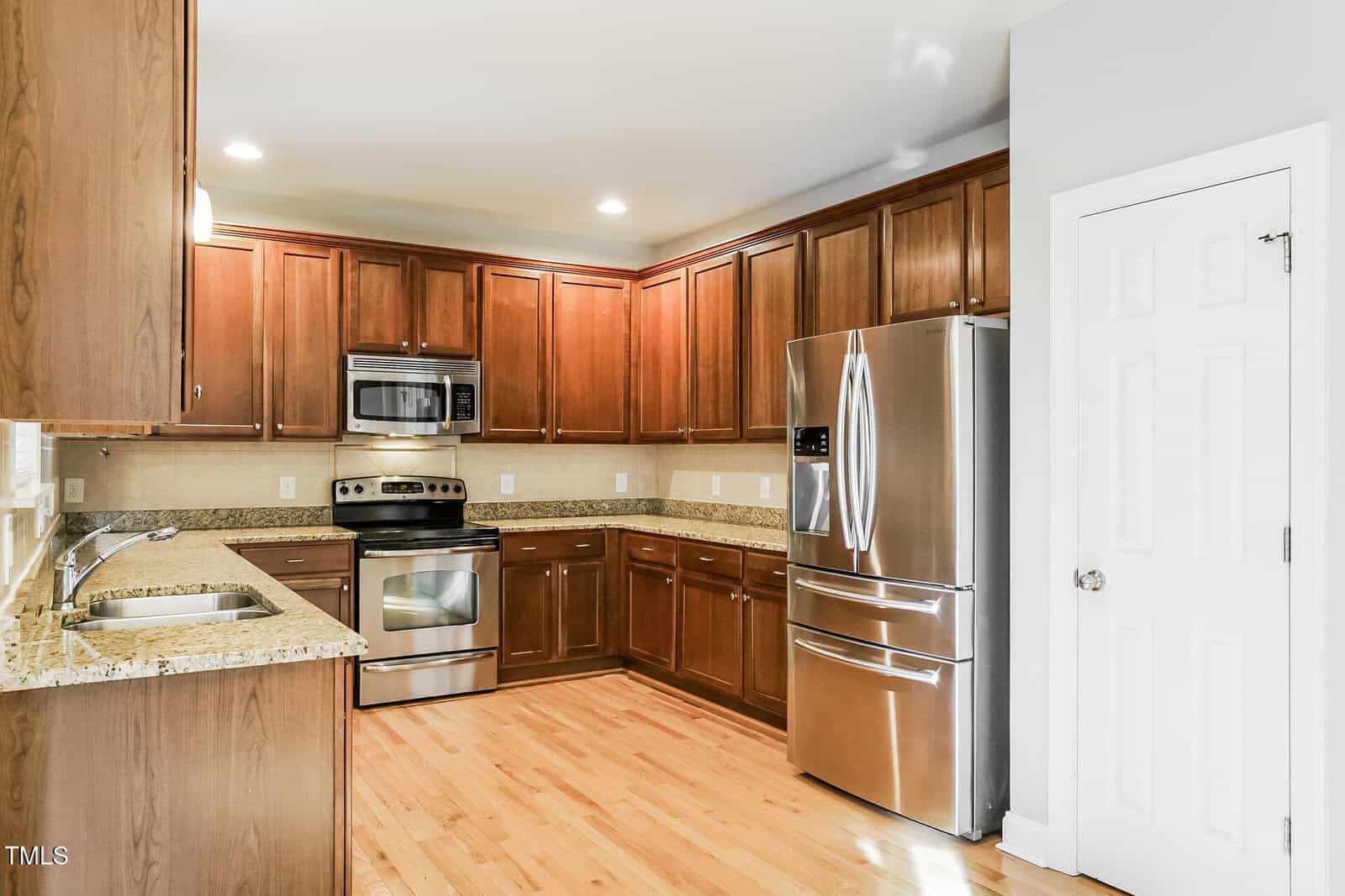 Kitchen with wooden cabinets, granite countertops, stainless steel appliances including refrigerator, oven, microwave, and dishwasher, light wood flooring, neutral wall color, and recessed ceiling lights.