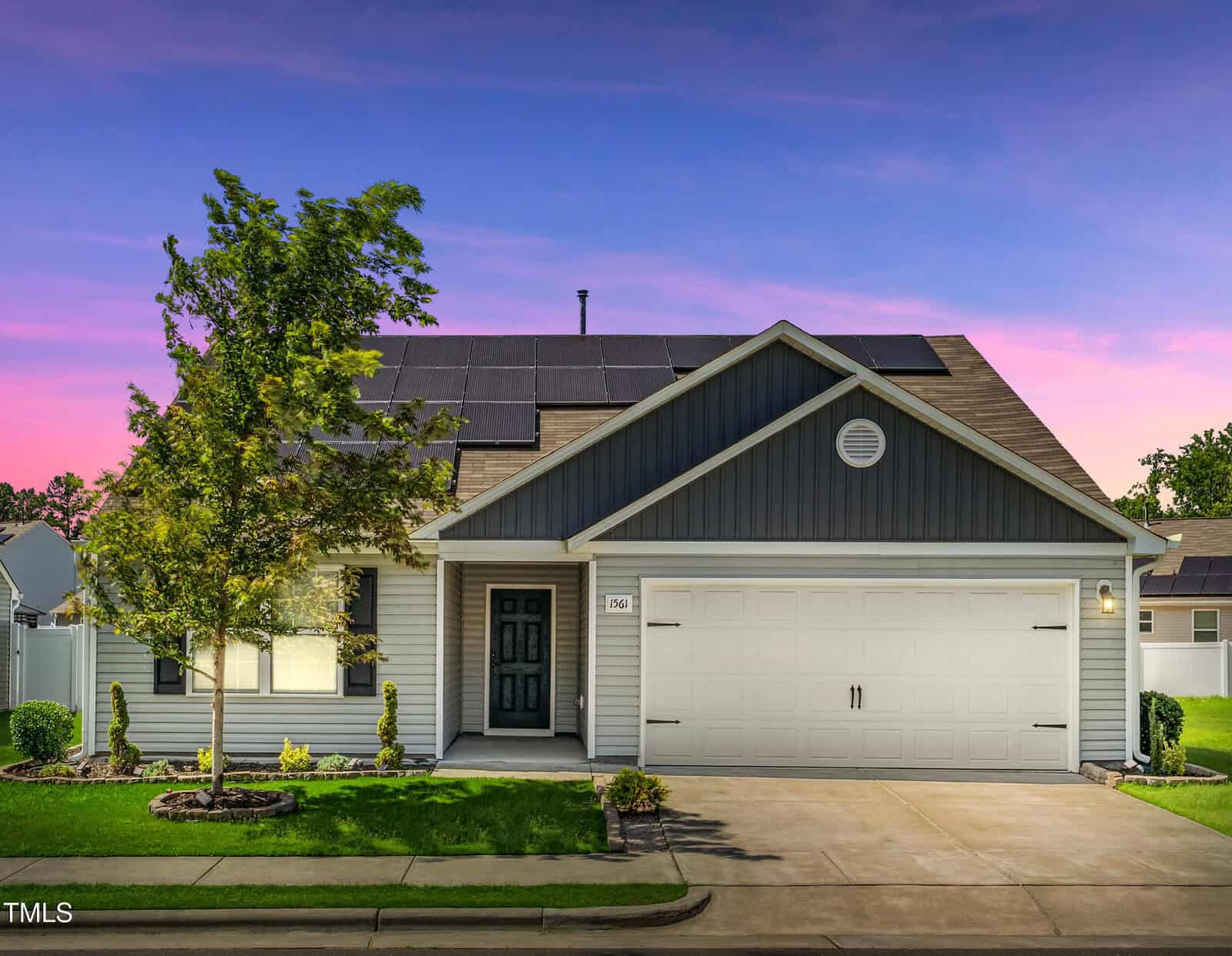 A single-story house at 1561 Dorsett Lane in Creedmoor with solar panels on the roof, gray siding, a covered entryway, white garage door, small front lawn, and a tree, photographed at sunset.