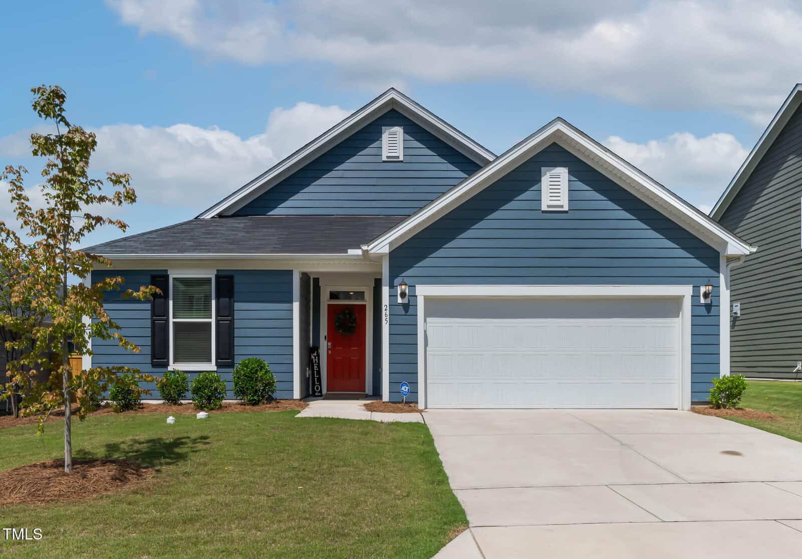 Located at 265 Purple Aster Street in Youngsville, this charming blue single-story house features white trim, black shutters, a vibrant red front door, and an attached two-car garage. The small front yard is beautifully landscaped with shrubs and a young tree, while the concrete driveway and sidewalk add to the home’s welcoming curb appeal.
