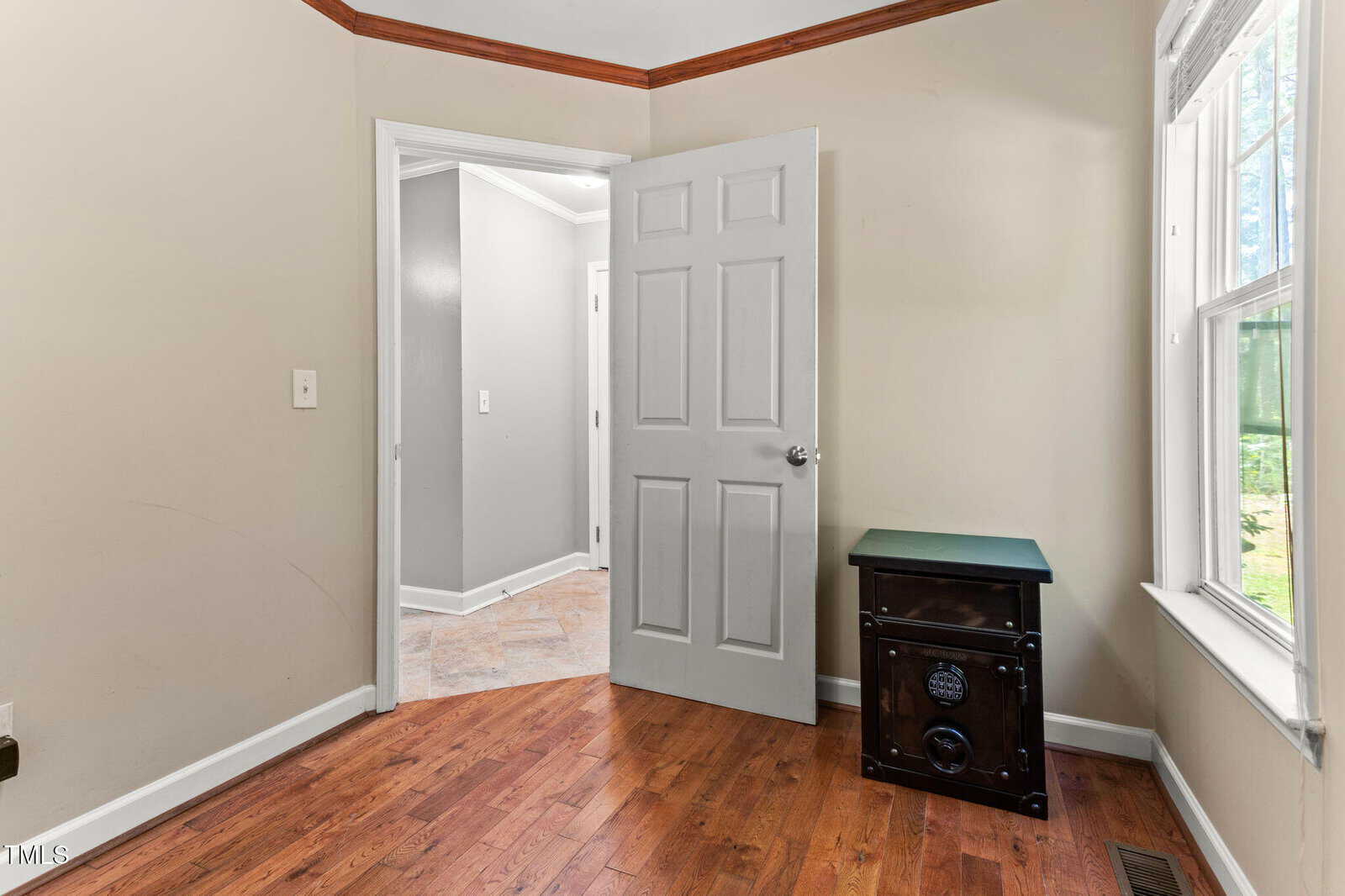 Small room with wood floor, beige walls, a white door partially open, and a window letting in natural light. A black electric heater sits in the corner near the window.