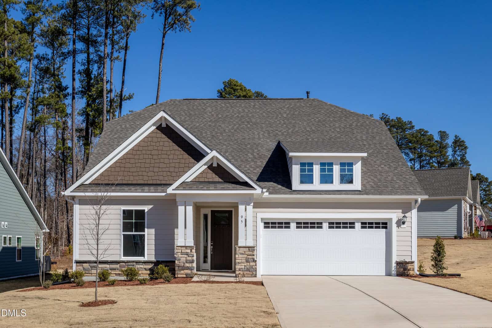 A modern single-story suburban house at 95 Bald Cypress Lane, Youngsville, with gray siding, stone accents, a covered front porch, and double garage sits on a dry, neatly landscaped lawn under a clear blue sky.