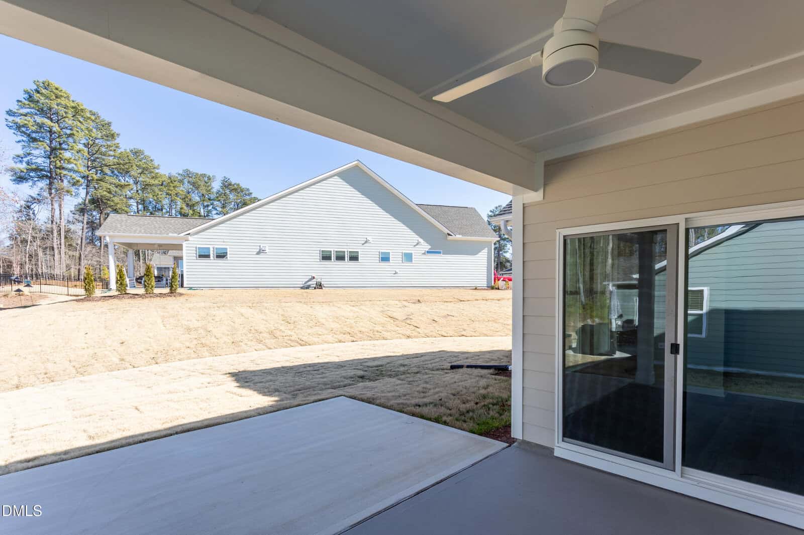 View from a covered patio with a ceiling fan, looking out onto a grassy backyard and a neighboring house in the background. Sliding glass doors lead inside the house.
