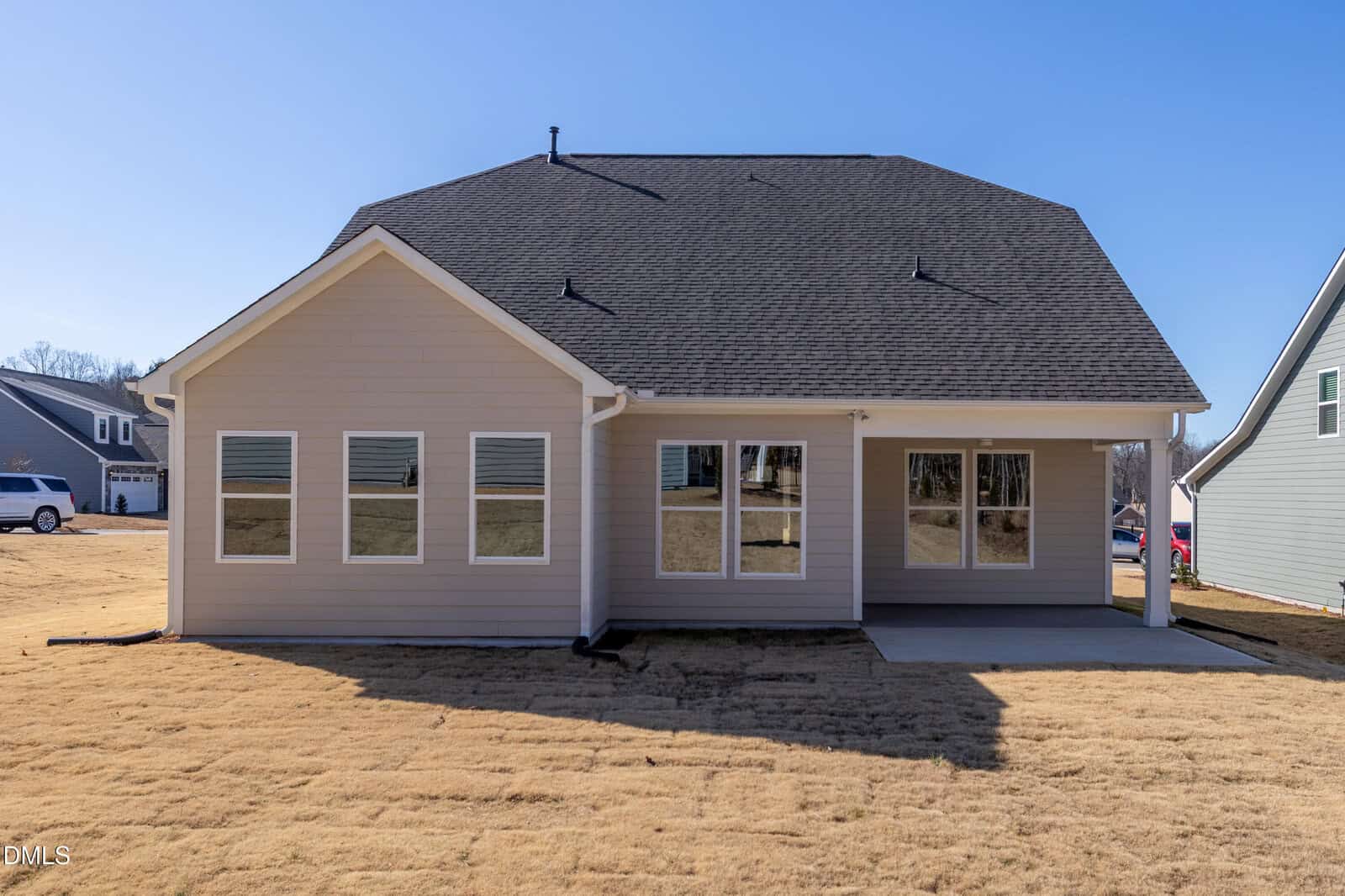 A modern house with light-colored siding, multiple windows, and a covered patio sits on a dry, yellowed lawn under a clear blue sky.