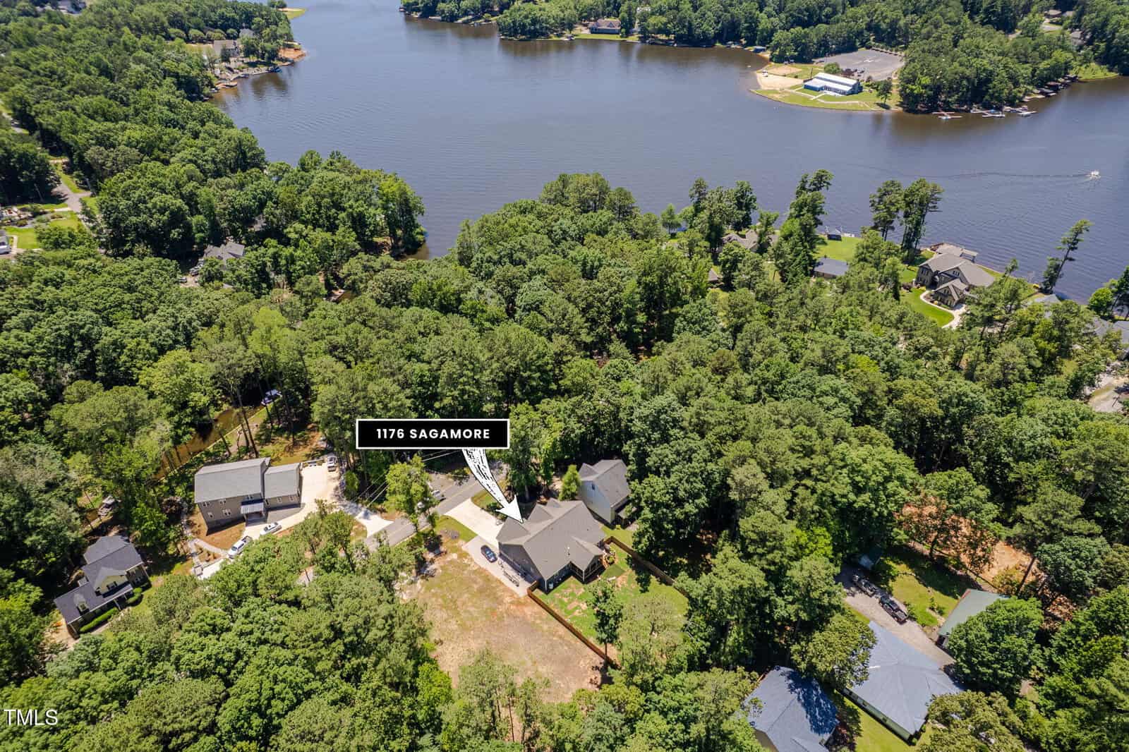 Aerial view of a wooded residential neighborhood by a lake in Louisburg, with a label pointing to a house and driveway identified as “1178 Sagamore.” Several homes—including one at 1176 Sagamore Drive—and a scenic shoreline are visible among the trees.
