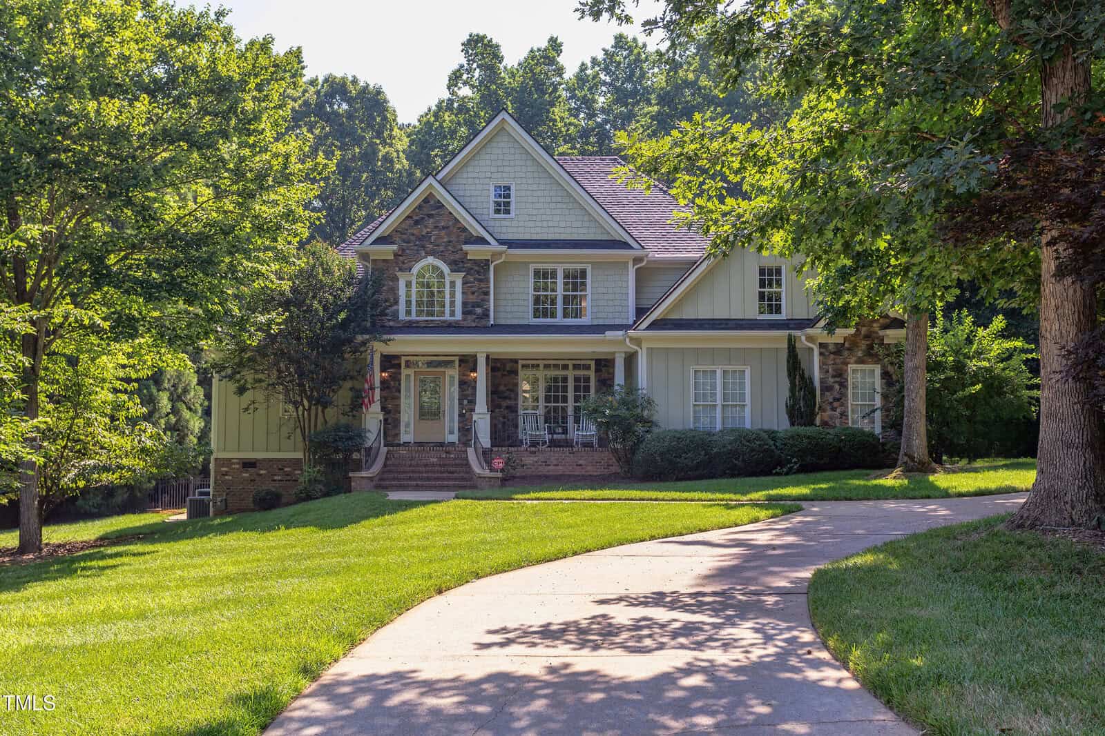 A large two-story house at 2012 Silverleaf Drive in Youngsville features beige siding, white trim, a front porch with chairs, and multiple windows, set behind a curved driveway and well-maintained lawn amidst tall trees and landscaping.