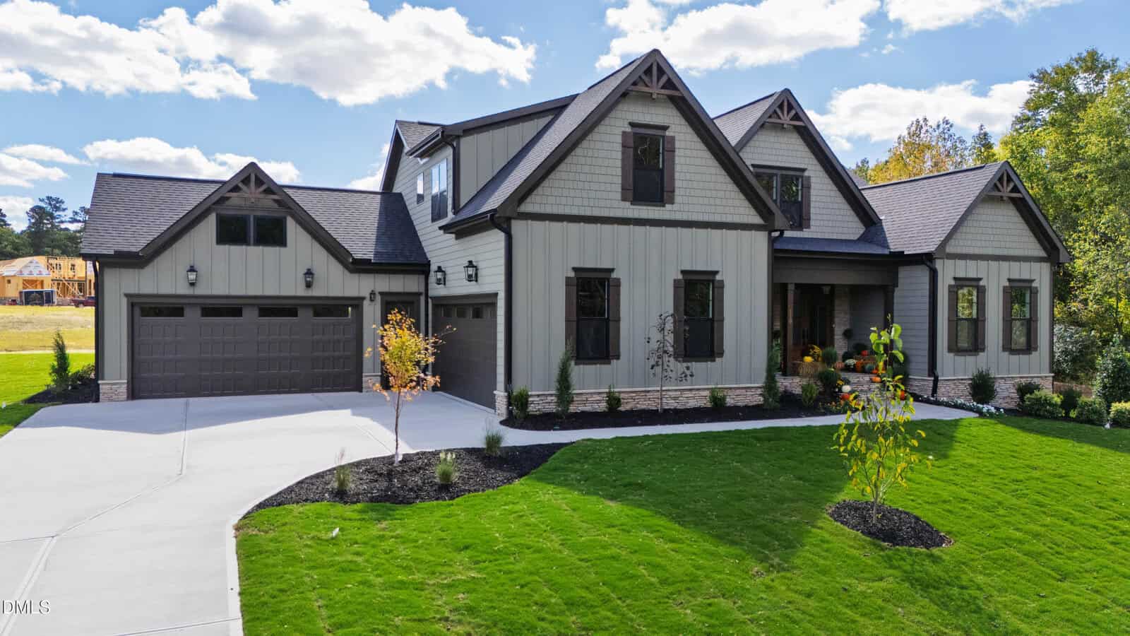 Two-story modern farmhouse with gray siding, dark trim, three-car garage, and gabled roof. Well-kept lawn, small trees, and clear sky with scattered clouds in the background.
