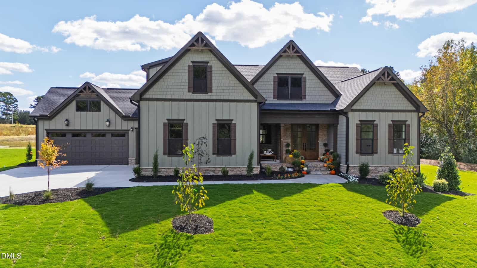 A two-story house with beige siding, dark trim, and a brick front porch, located at 110 Broadleaf Lane in Youngsville. The home features a two-car garage, manicured lawn, small trees, and pumpkins by the entrance. The sky is partly cloudy.
