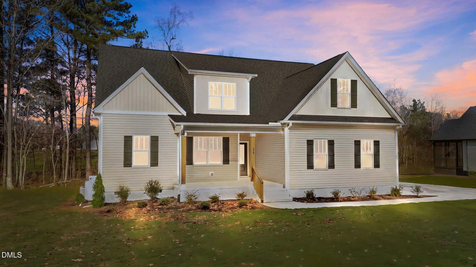 A modern beige house with black shutters, white trim, and a front porch sits on a green lawn at sunset at 25 Autumnwood Lane in Spring Hope, surrounded by trees and landscaped bushes.