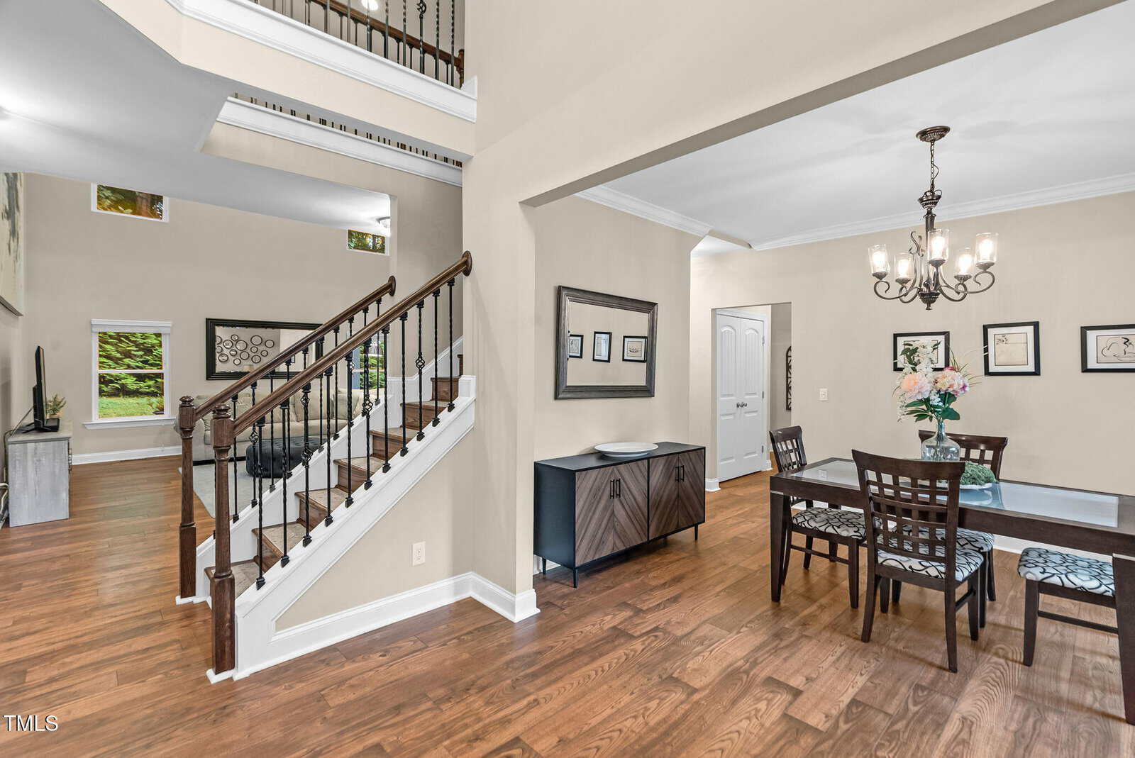 Open dining area with a dark wood table and chandelier, adjacent to a staircase with white trim and wooden railing, leading to an upper floor in a modern home with hardwood floors.