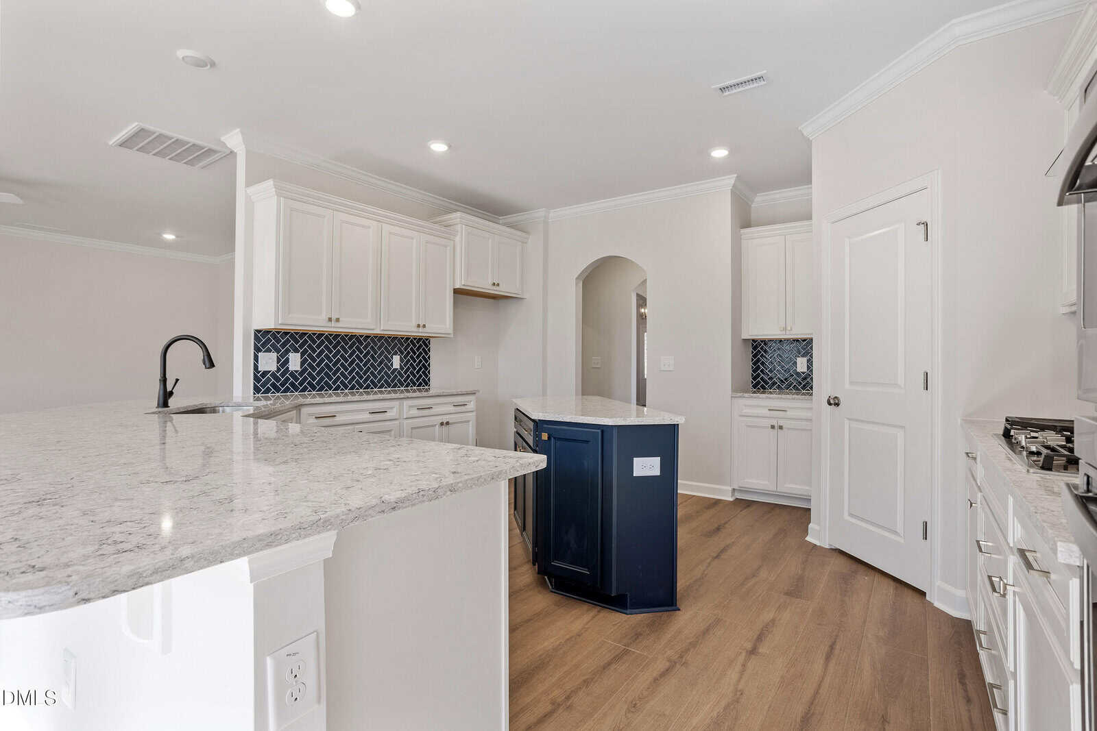 A modern kitchen with white cabinets, marble countertops, a small dark blue island, stainless steel appliances, a black faucet, wood flooring, and a blue patterned tile backsplash.