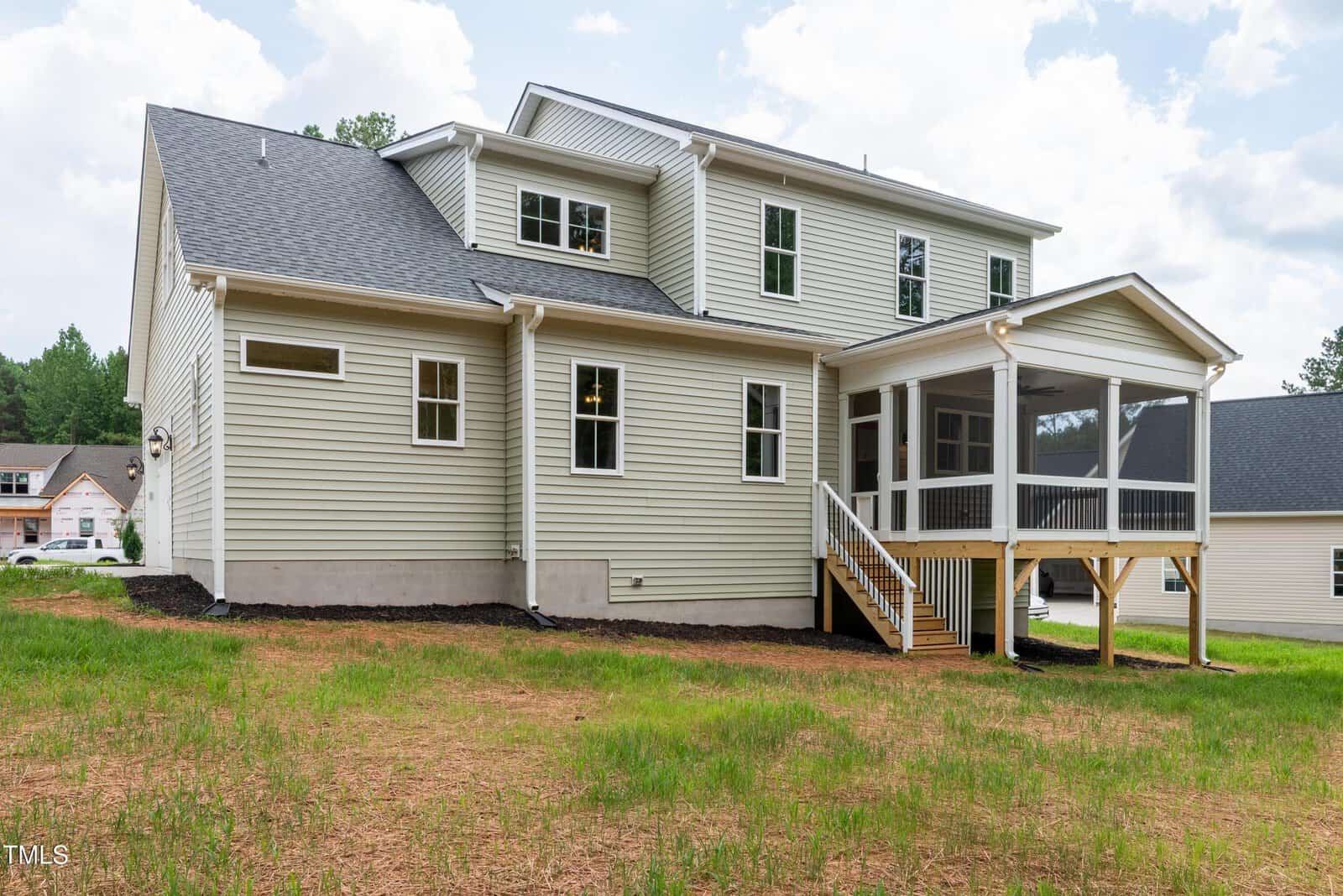 Two-story beige house with white trim, multiple windows, and a screened-in porch on the back, wooden steps leading to the porch, and a grassy yard with patches of bare soil.
