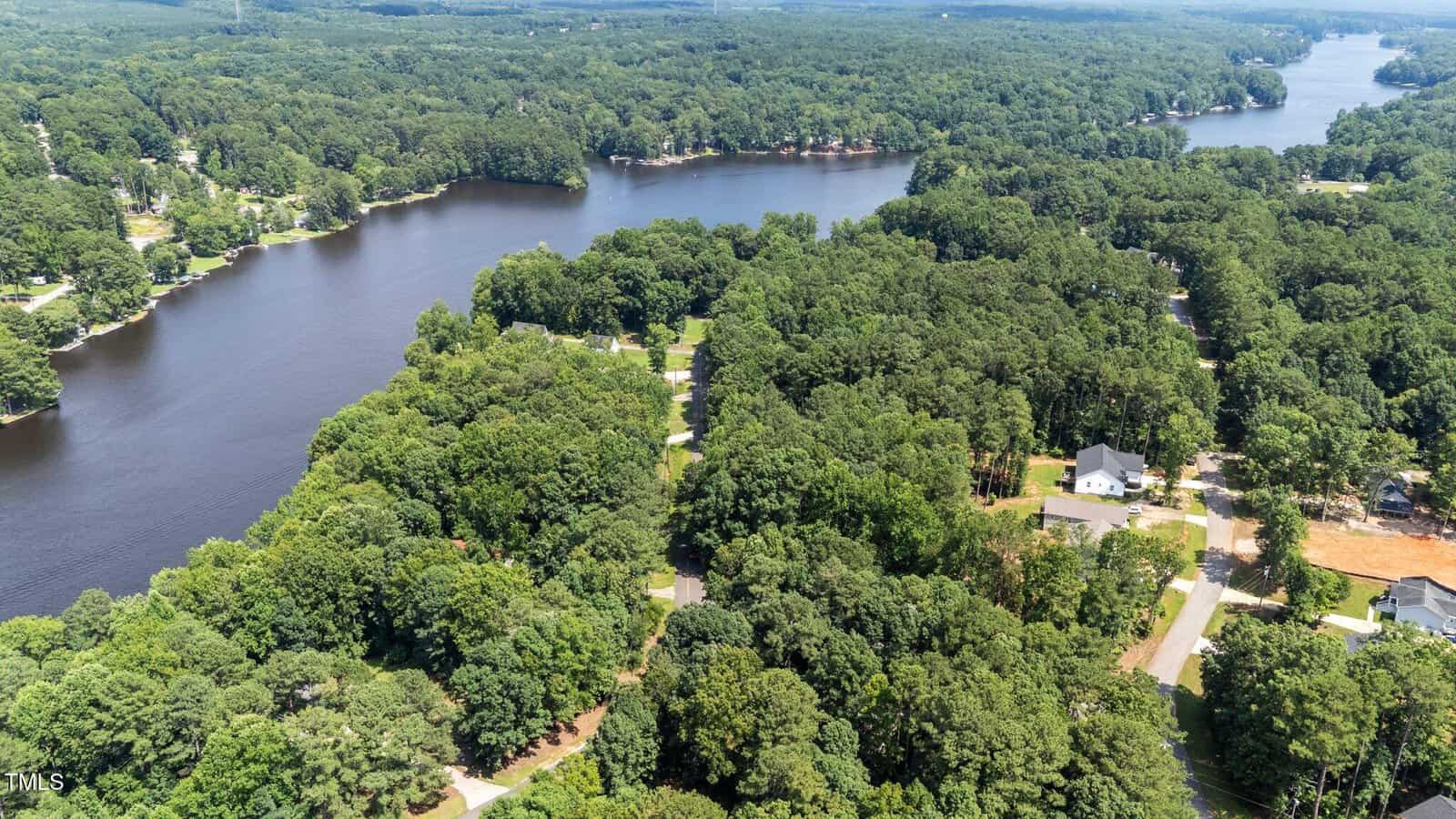 Aerial view of a tree-covered residential area beside a winding river or lake, with scattered houses visible among the greenery and a road running through the neighborhood, including 104 Lone Star Drive in Louisburg.