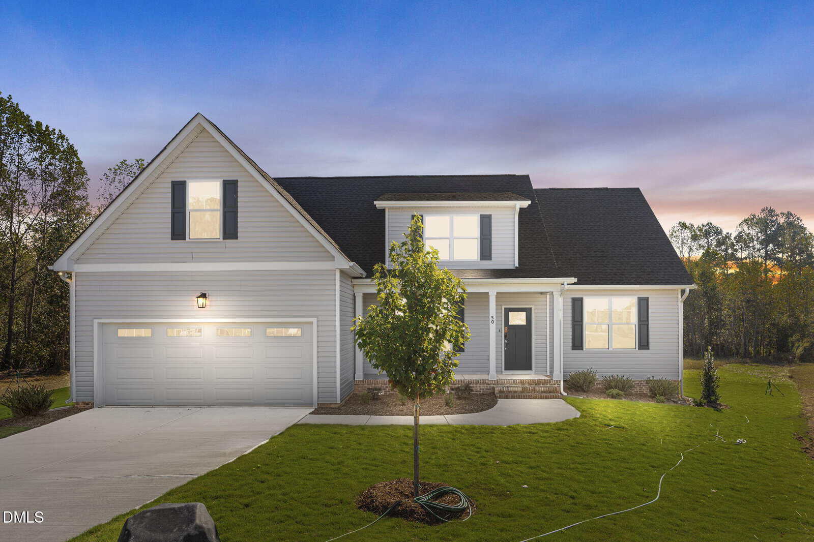 A modern, two-story gray house with white trim and a black roof, featuring a double garage, a front porch, and a small tree in a well-kept lawn at sunset.
