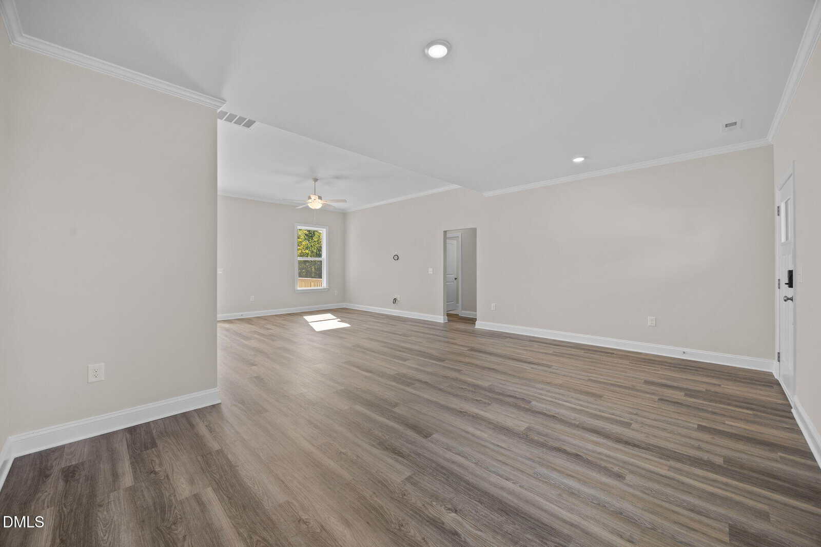 Spacious empty room with light wood flooring, white walls, ceiling fan, recessed lighting, and a window letting in natural light. Multiple doorways are visible.