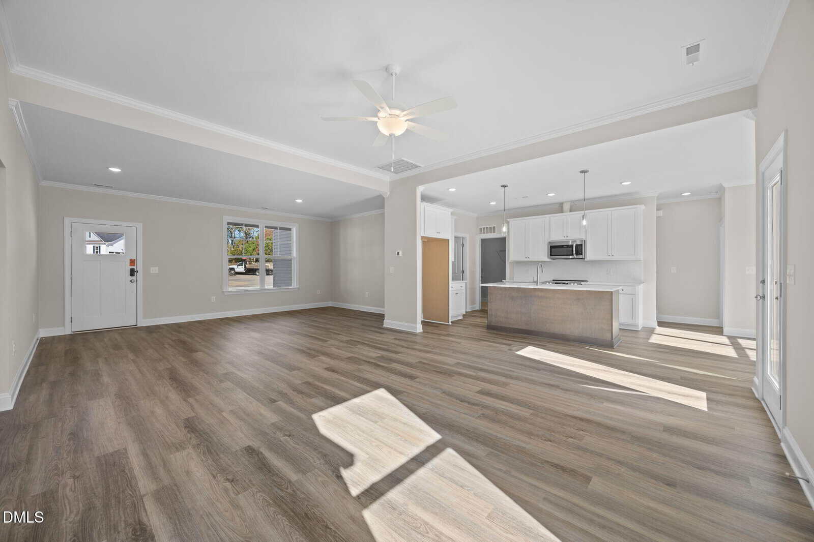 Spacious, modern open-concept living area with wood-style floors, neutral walls, ceiling fan, large windows, and a kitchen featuring white cabinets, stainless steel appliances, and an island with pendant lights.