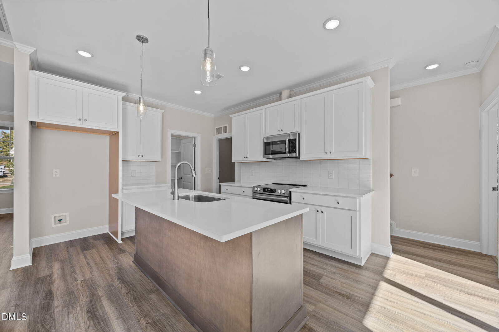 Bright modern kitchen with white cabinets, stainless steel appliances, a built-in microwave, and an island with a sink; wood-style flooring and pendant lights complete the clean, open design.