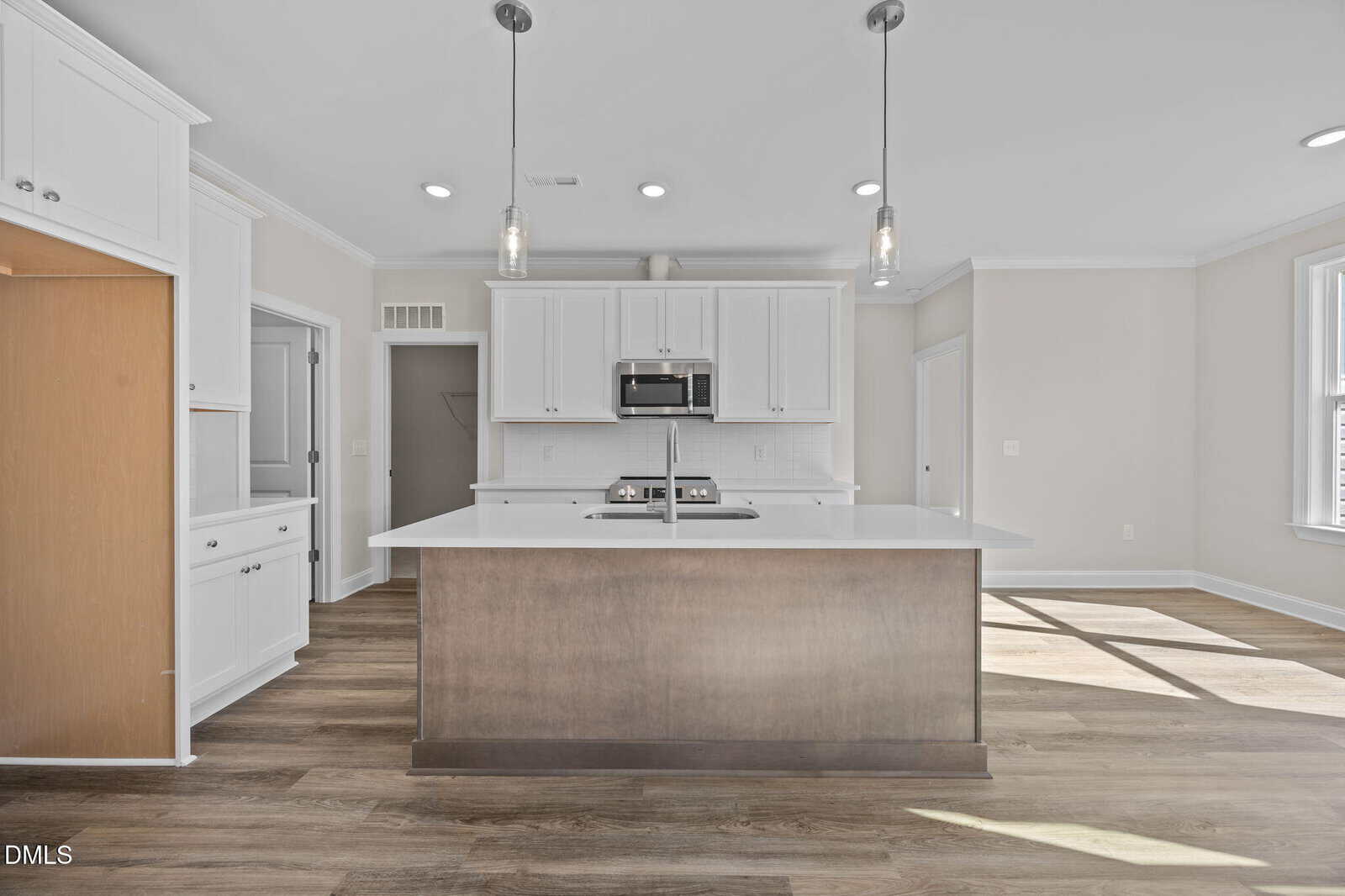 Modern kitchen with white cabinets, stainless steel appliances, and a large center island with a wood base. Pendant lights hang above the island, and the room features light walls and wood-style flooring.