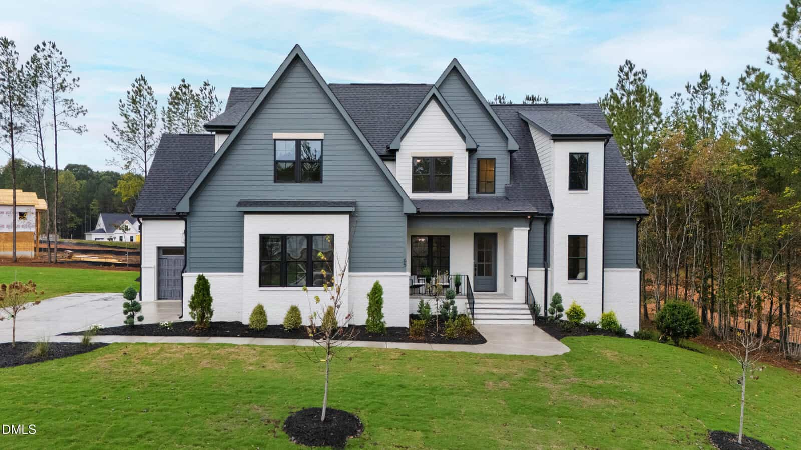 Modern two-story house with gray siding and white brick exterior at 65 Spanish Oak Drive, Youngsville. Large front windows, black roof, front porch with steps, and a neatly landscaped lawn with young trees. Pines and other houses in the background.