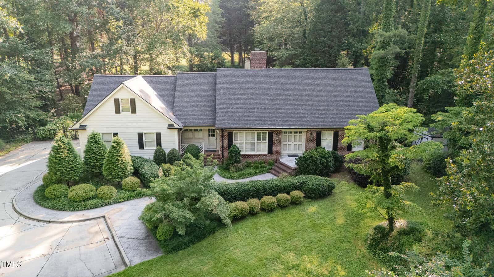 The Henderson home at 515 S Woodland Road is a two-story suburban house with a gabled roof and brick siding, surrounded by manicured bushes, trees, and a curved driveway leading to the entrance in a wooded area.