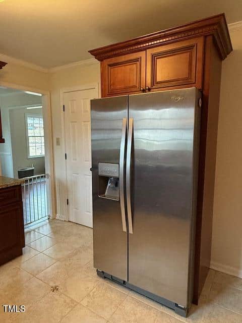 A stainless steel side-by-side refrigerator with an external water and ice dispenser is positioned between a kitchen wall and a wooden cabinet, on a tiled floor. An open doorway is visible in the background.