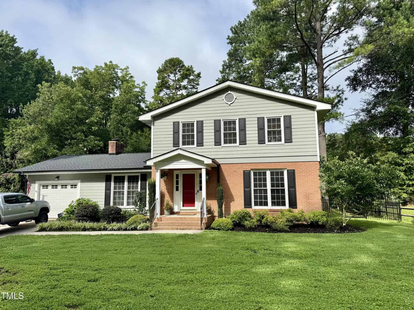 A two-story house at 138 Dorsey Place, Henderson, features gray siding, black shutters, and a brick lower facade. A red front door, attached garage, green lawn with shrubs, tall trees, and a wooden fence complete the setting.