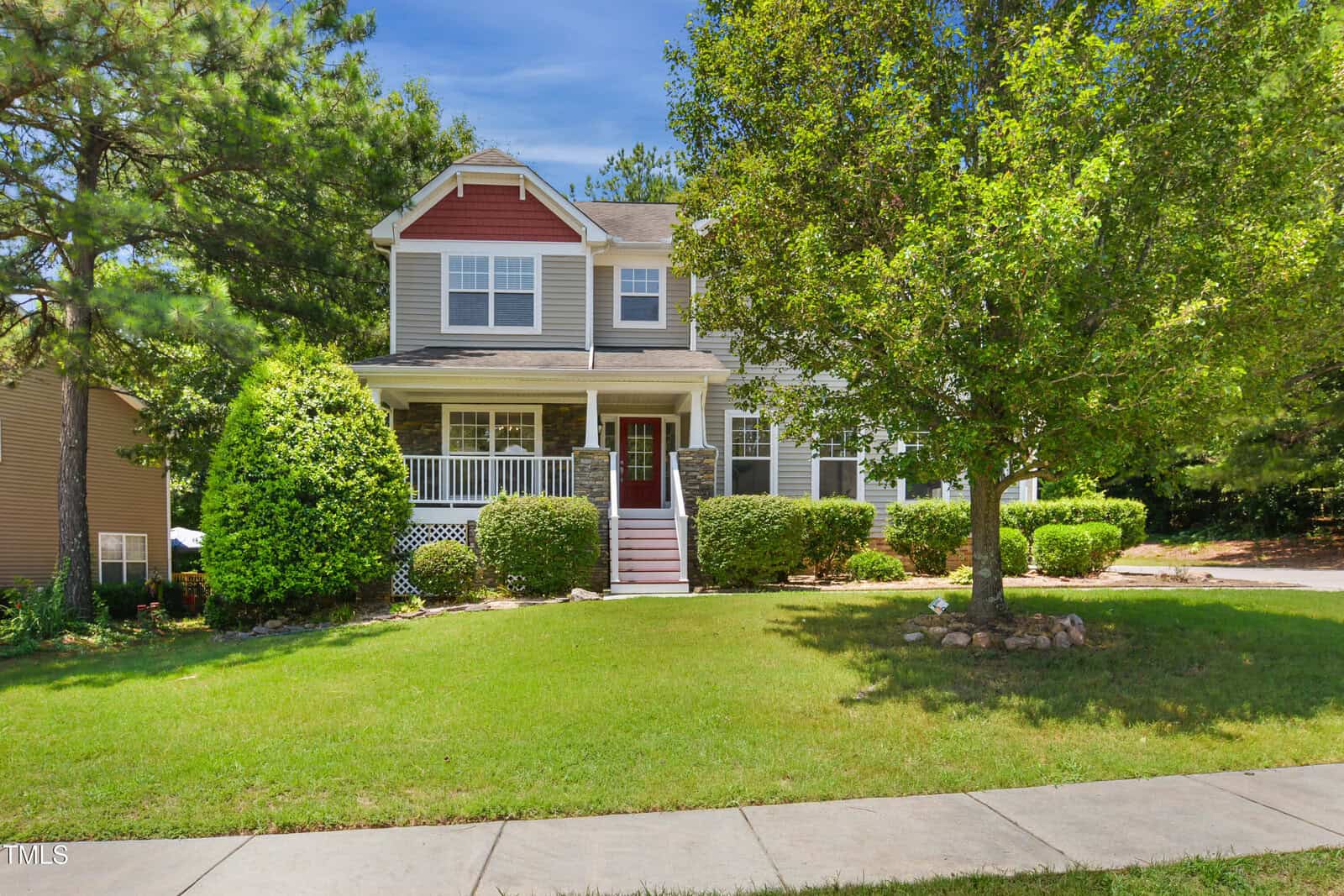 Two-story suburban house with a front porch, red door, and white trim, surrounded by green shrubs and trees at 80 Clubhouse Drive in Youngsville. The lawn is neatly maintained, and a sidewalk runs along the front of the property on a sunny day.