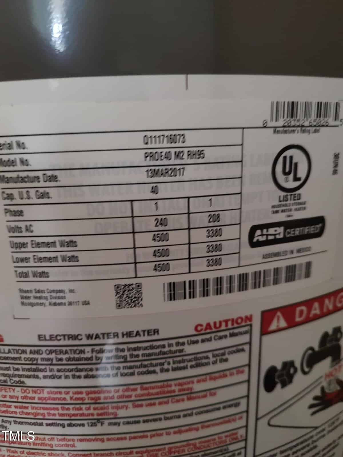 Close-up of a water heater label showing model number, manufacture date, capacity, voltage, wattage, and certification details, with safety warnings partially visible at the bottom of the label.