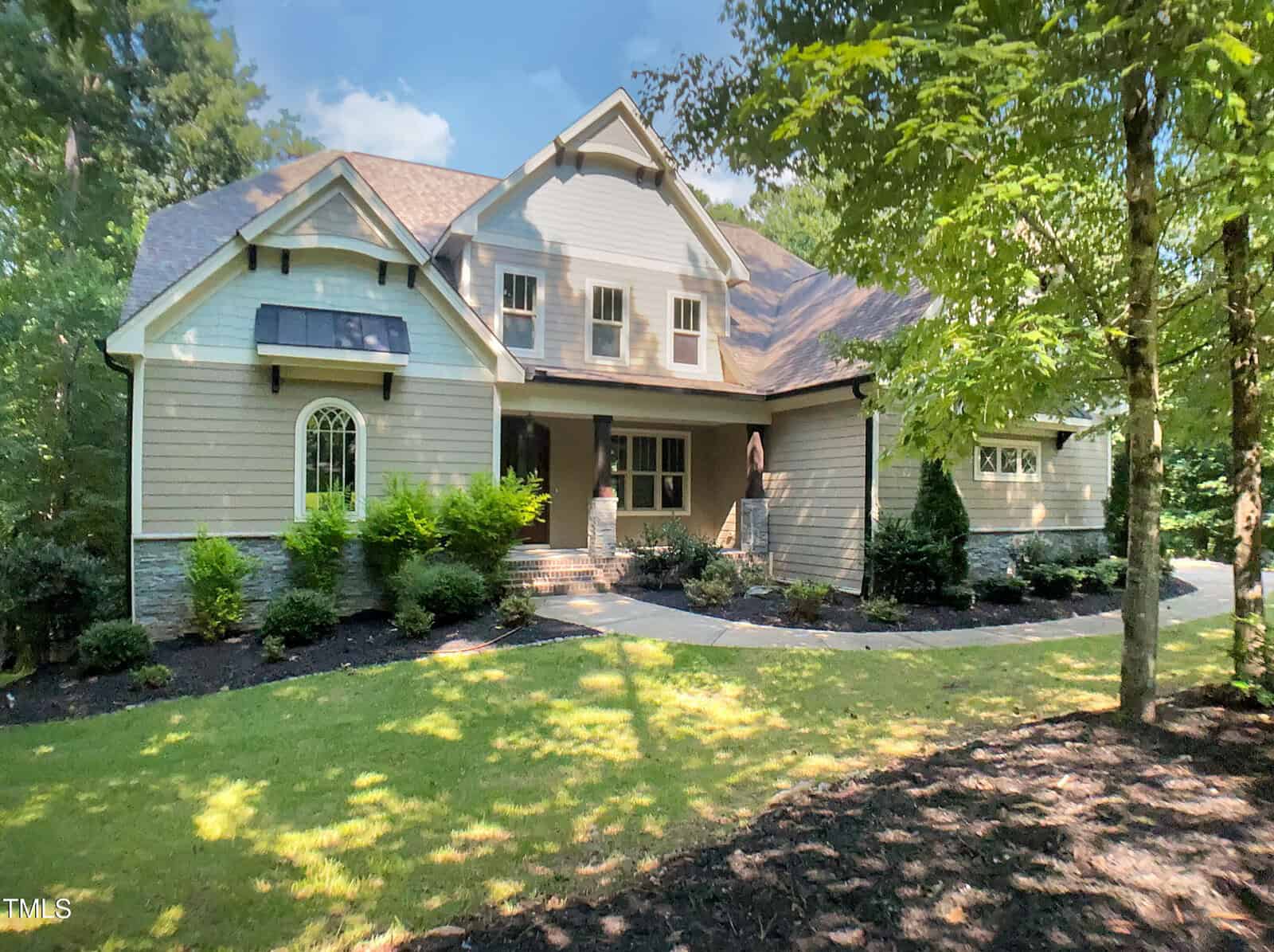 A two-story suburban house at 3575 Bragg Valley Lane in Wake Forest features beige siding, stone accents, and a dark roof, nestled behind a curved sidewalk amid green shrubs, manicured lawn, and trees on a sunny day.