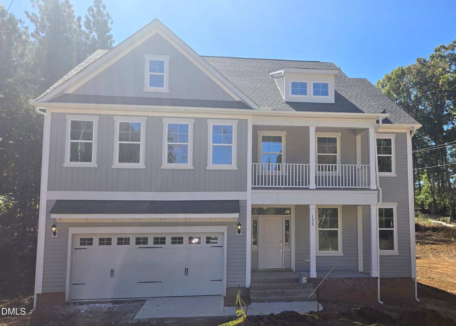 Two-story gray house with white trim, double garage, multiple windows, a small upper balcony, and a covered front entry located at 135 Guardian Street in Youngsville. The yard appears unfinished, with dirt and some construction materials visible.