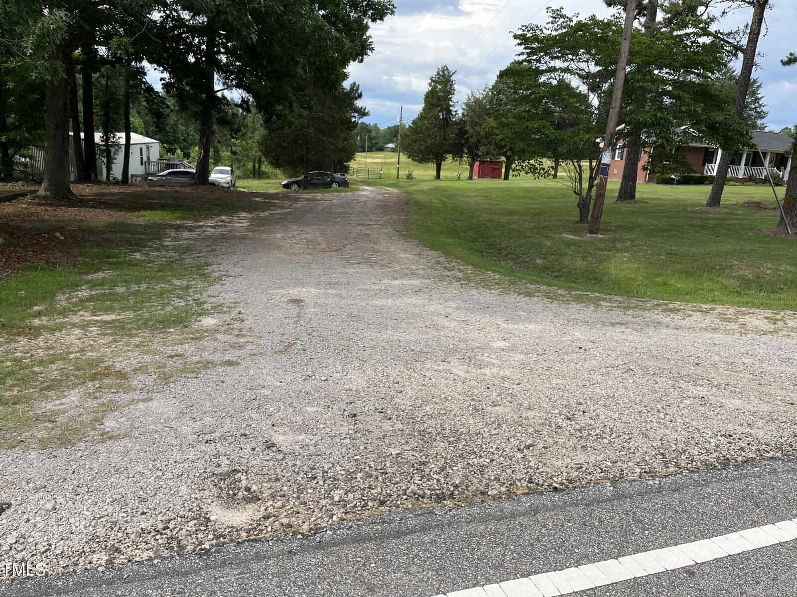 A gravel driveway off 00 Bullocksville Park Road in Manson leads into a grassy yard with trees. A white mobile home and a brick house are visible, along with parked cars and a red shed in the background.