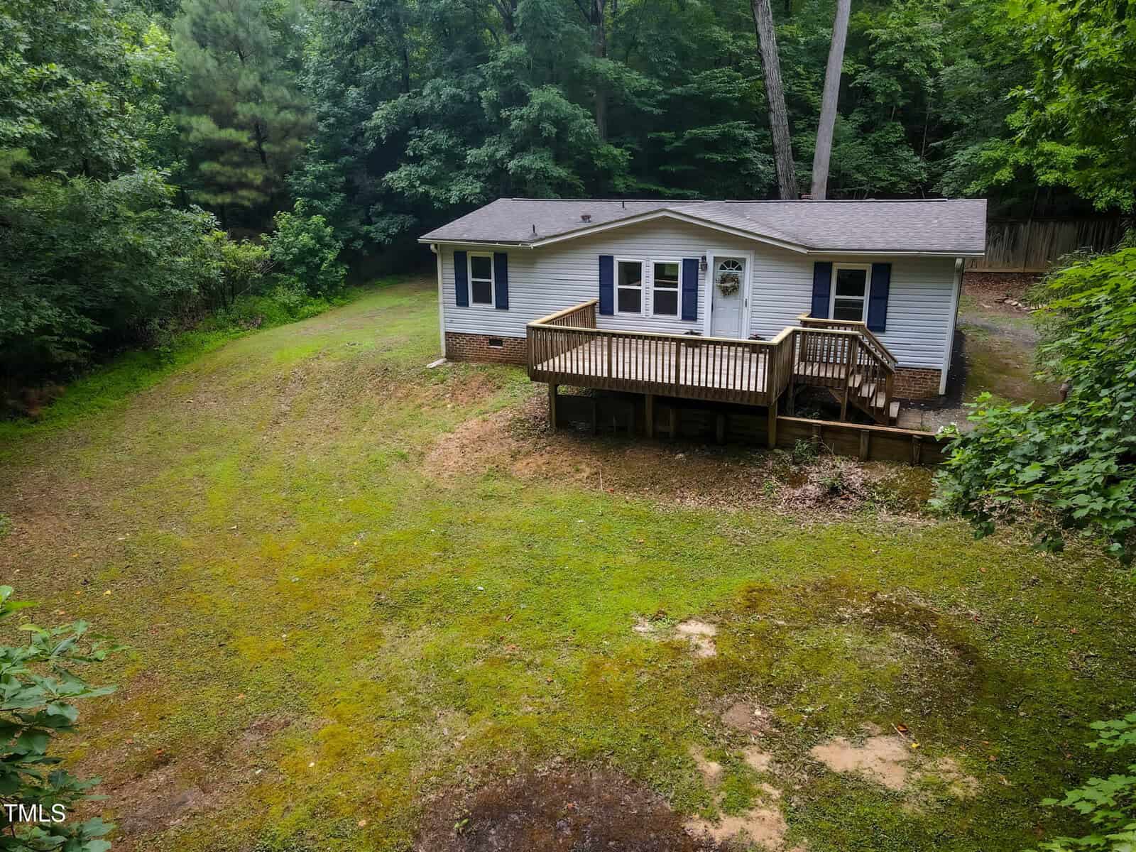 A small, single-story white house with a front porch and wooden steps sits on a grassy plot at 3146 Virginia Pine Court in Wake Forest, surrounded by trees and dense greenery. The yard is slightly sloped and partially bare in places.
