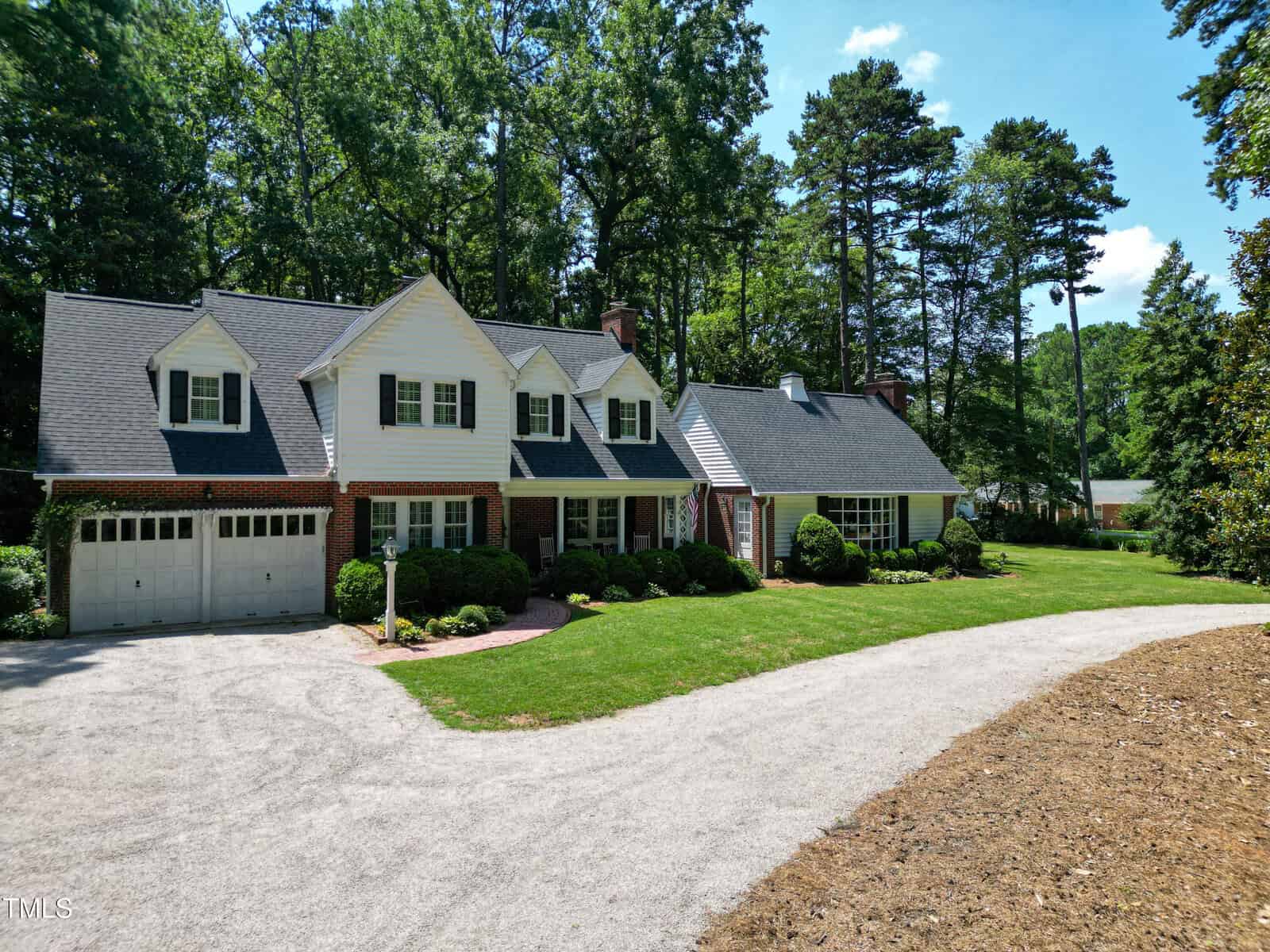 Two-story brick and white siding house with attached garage, located at 2945 Oxford Road in Henderson, surrounded by green bushes and tall trees, on a sunny day with a curved gravel driveway in front.