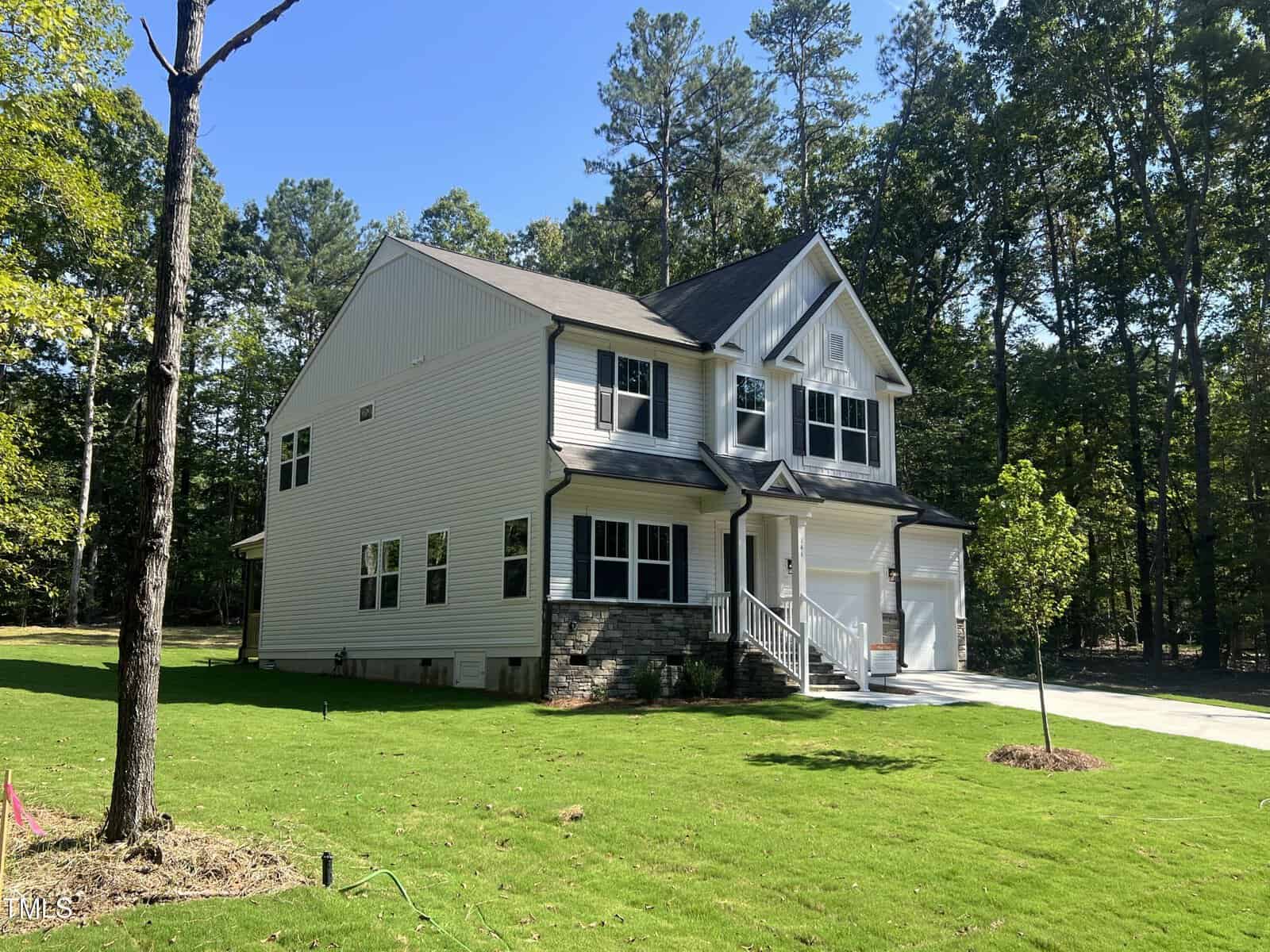 A two-story house with light-colored siding, dark roof, attached double garage, and stone accents on the front, surrounded by green lawn and trees under a clear sky.