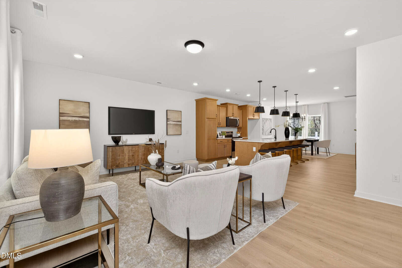 Modern open-concept living room and kitchen with neutral tones, plush seating, TV, wooden dining table, pendant lights, and natural light from large windows.
