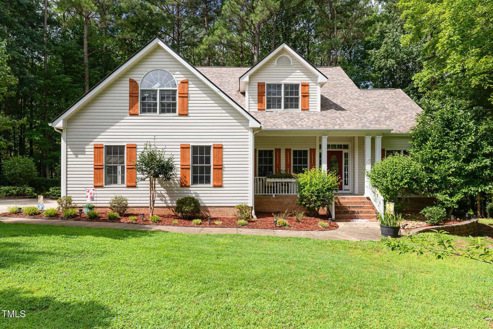A two-story suburban house at 235 Highview Drive in Youngsville with white siding, brown window shutters, a cozy front porch, and a well-kept lawn bordered by mulch and shrubs, surrounded by trees in the background.