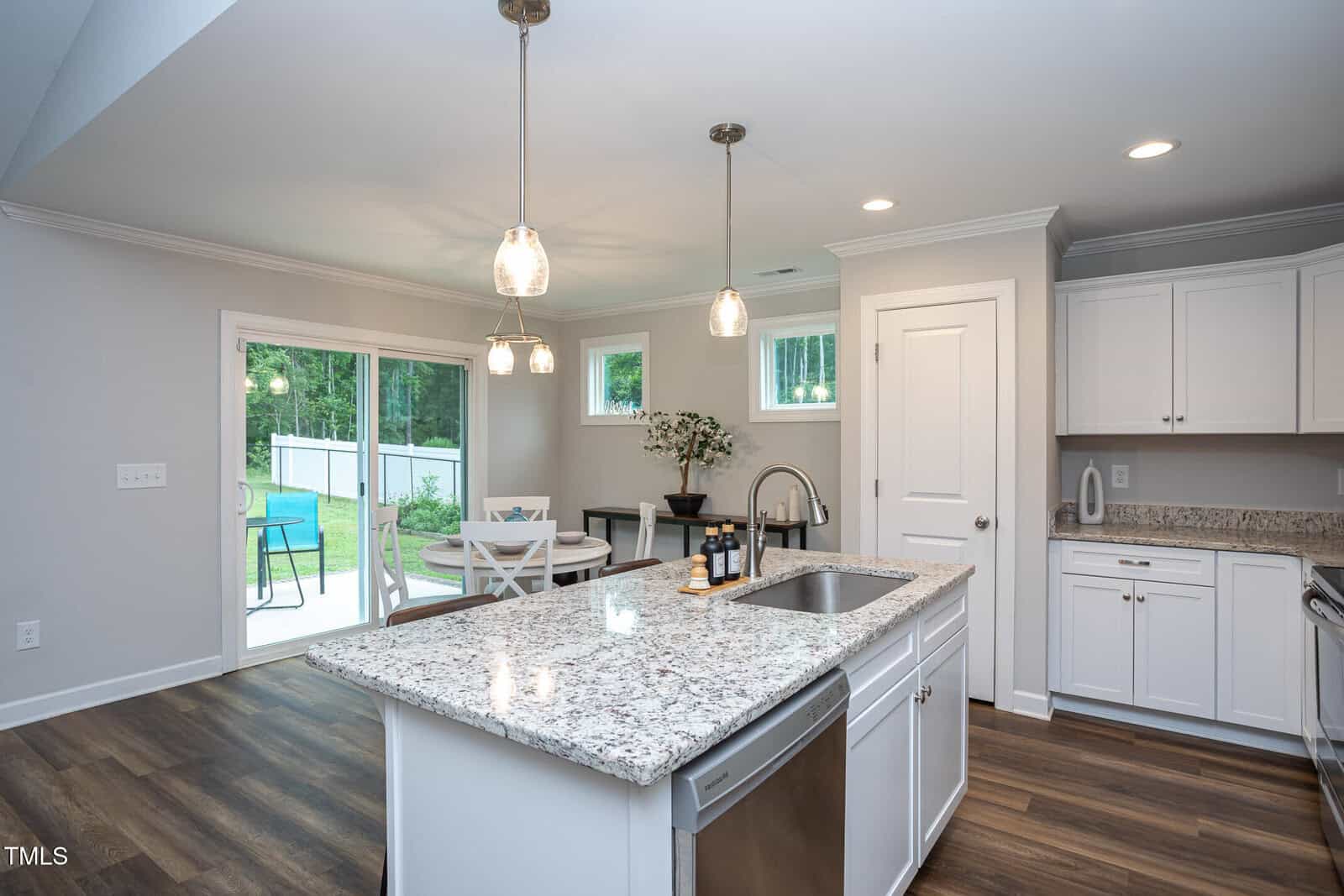 Modern kitchen with white cabinets, granite countertops, stainless steel appliances, and pendant lights over an island; adjoining dining area beside sliding glass doors overlooking a fenced backyard with a pool.