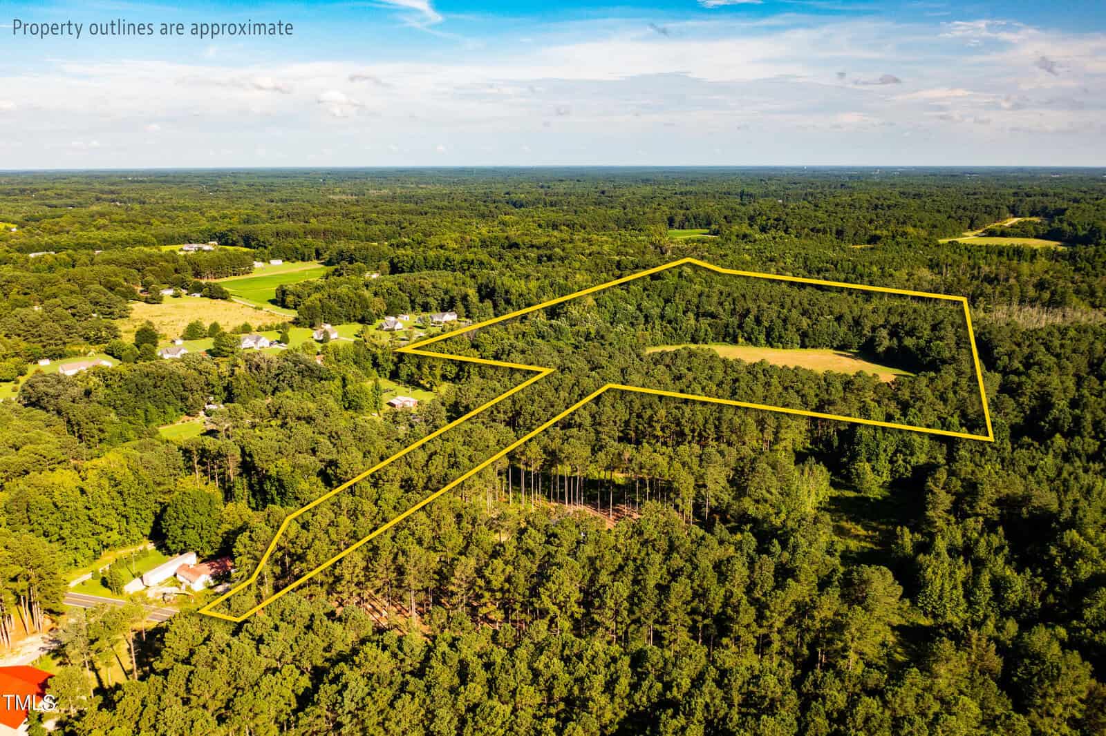 Aerial view of a rural, wooded landscape with a yellow outline marking the approximate boundaries of a large property surrounded by trees and scattered houses under a blue sky.
