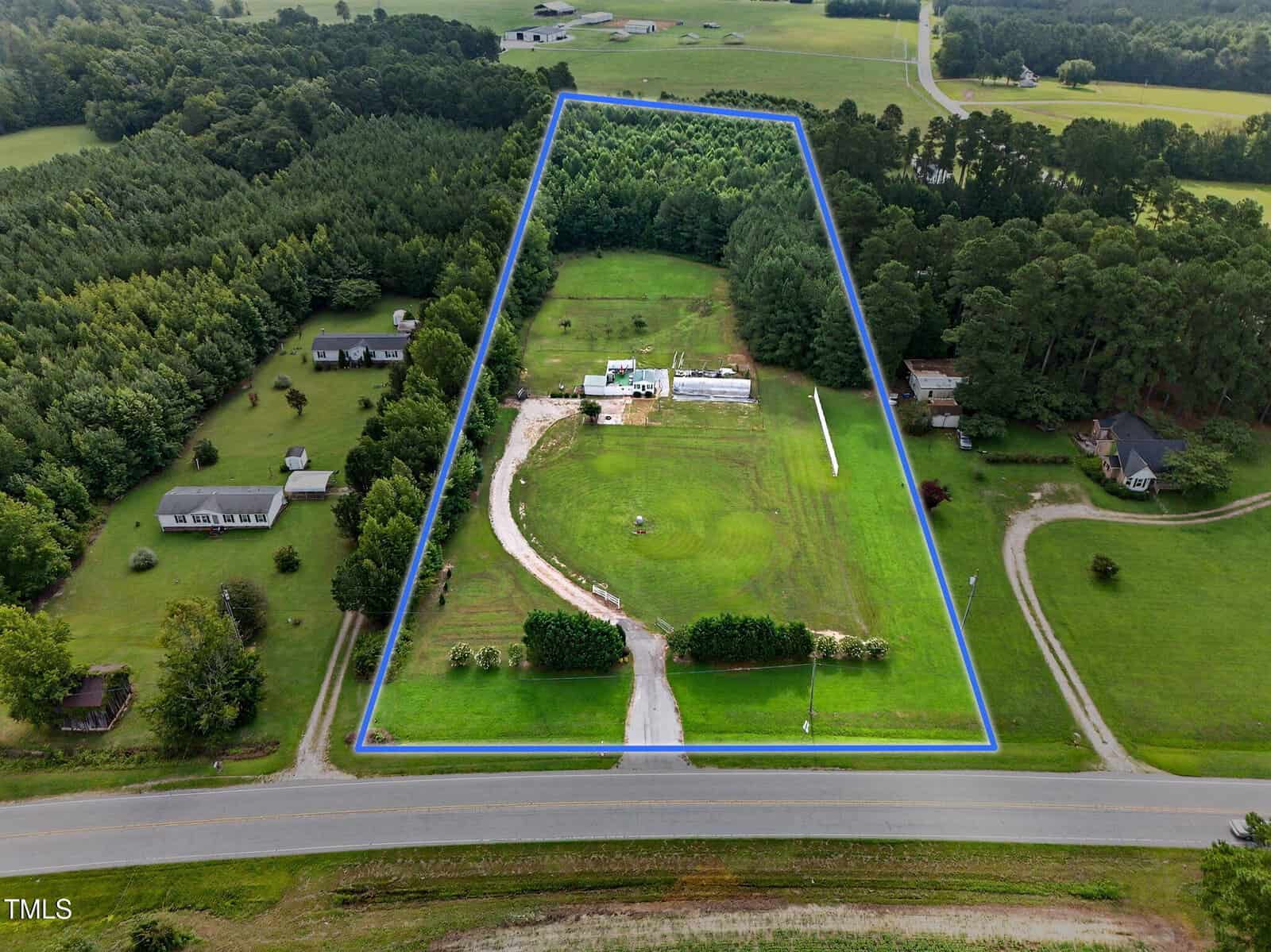 Aerial view of a rectangular plot of land outlined in blue at 4482 N Hwy 39, Louisburg, featuring a driveway, several structures, and open grassy areas, surrounded by trees and neighboring homes in a rural setting.